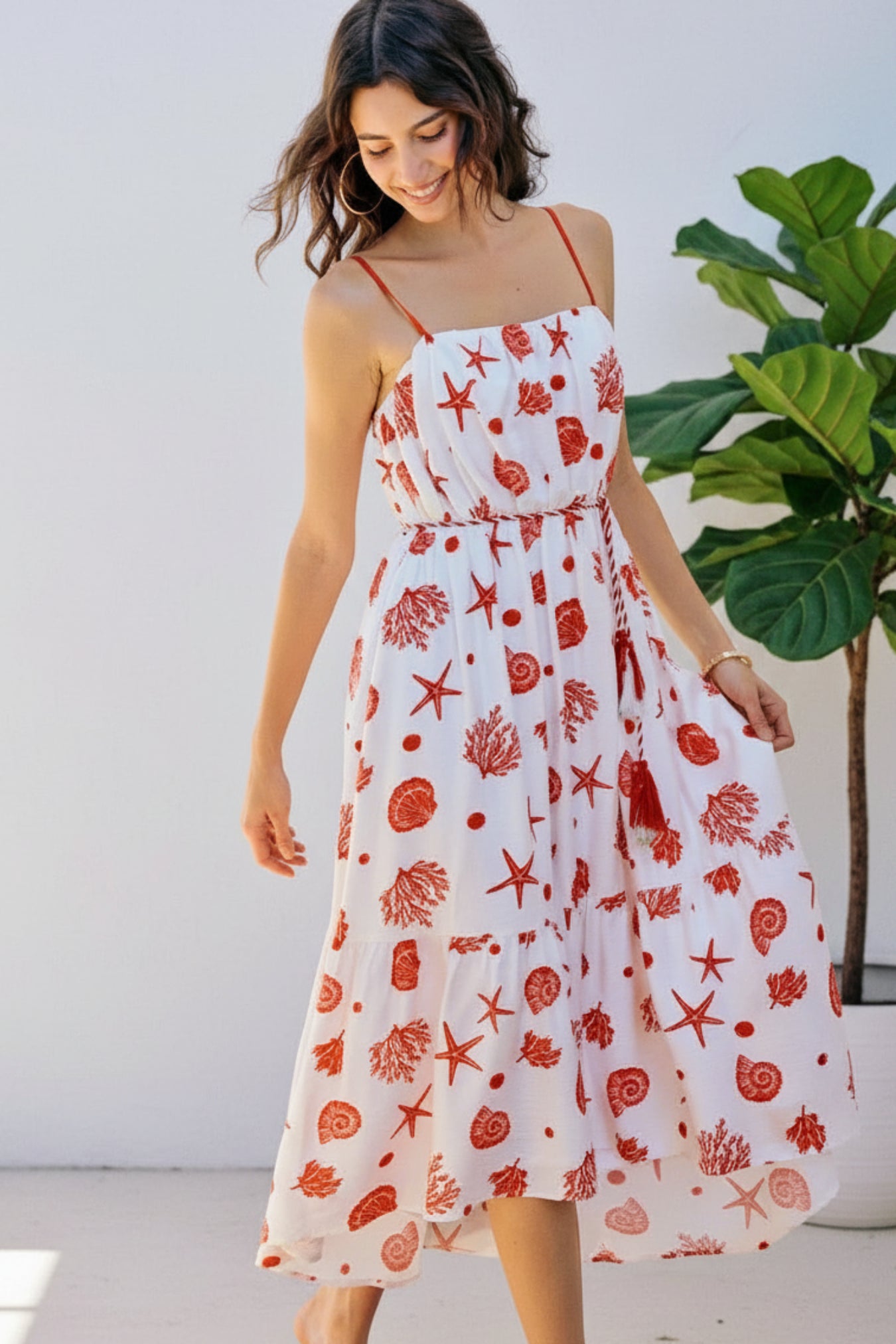 Woman wearing a white dress with red floral patterns standing outside.