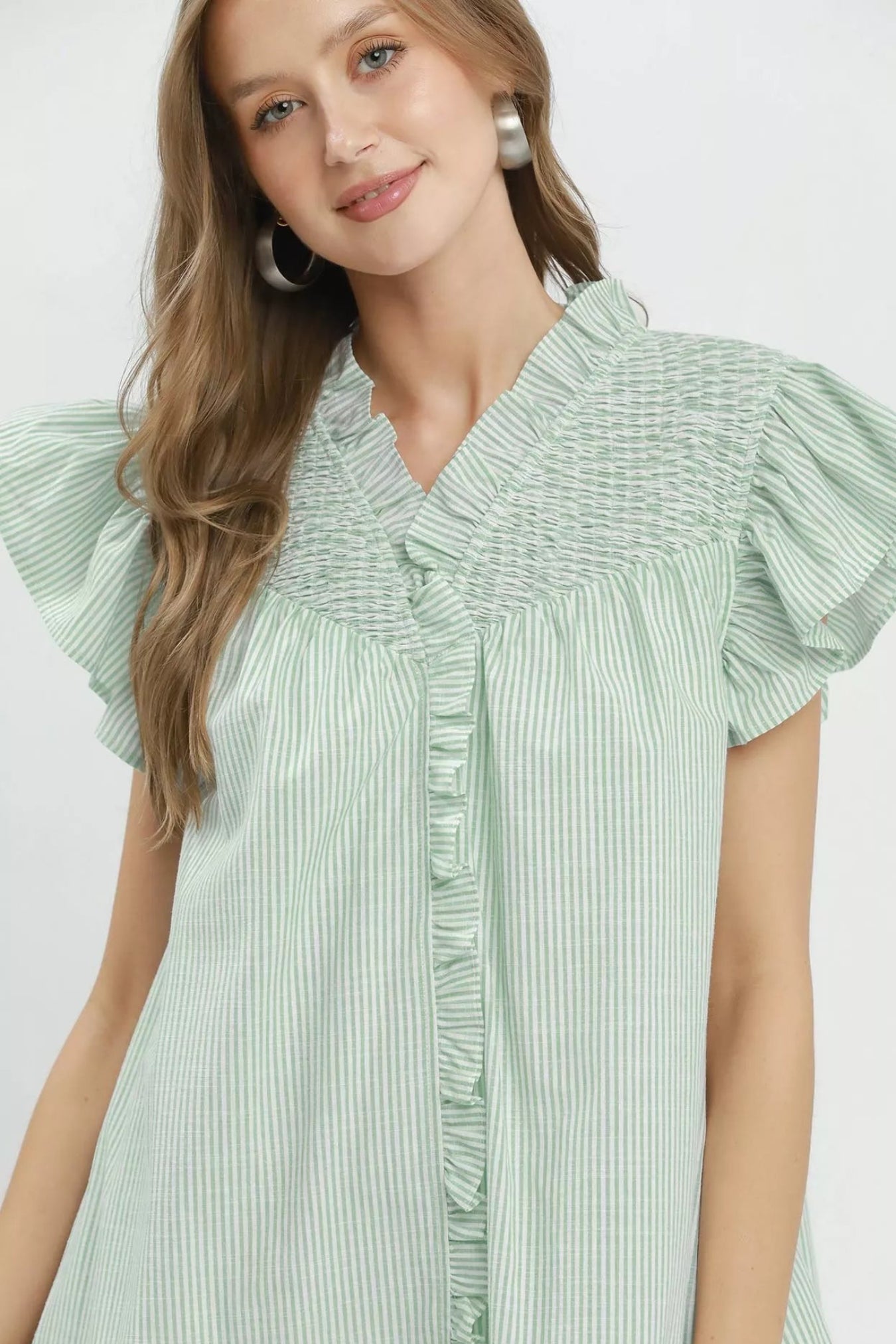 Woman wearing a light green dress with ruffled sleeves on a white background