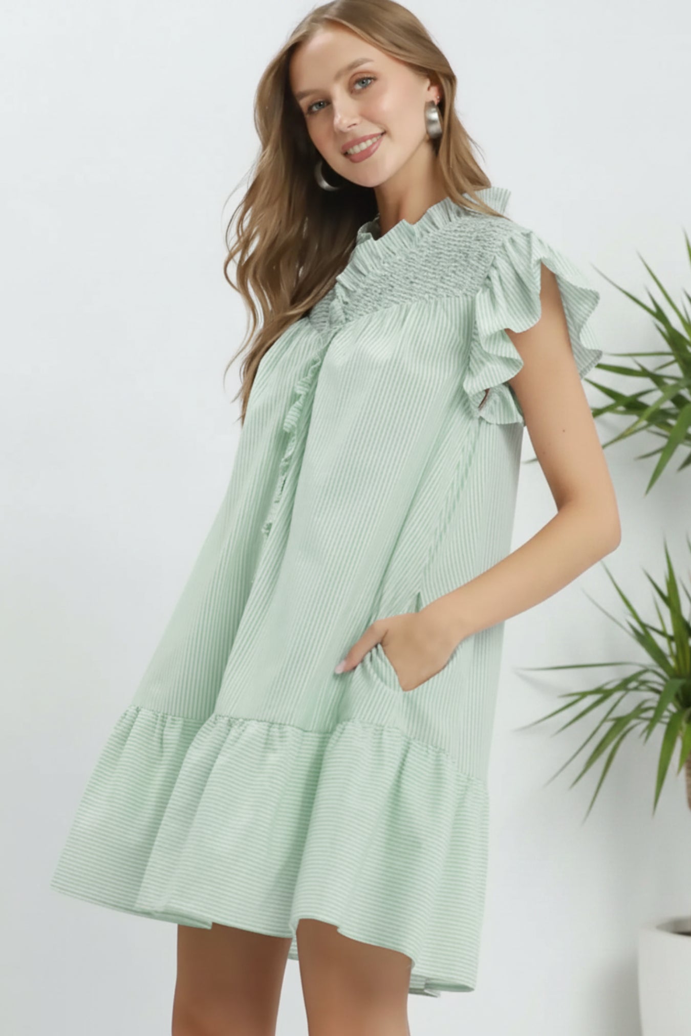 Woman wearing a light green dress with ruffled sleeves on a white background