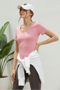Woman wearing a pink top, white shirt tied around her waist, and white cap on a white background