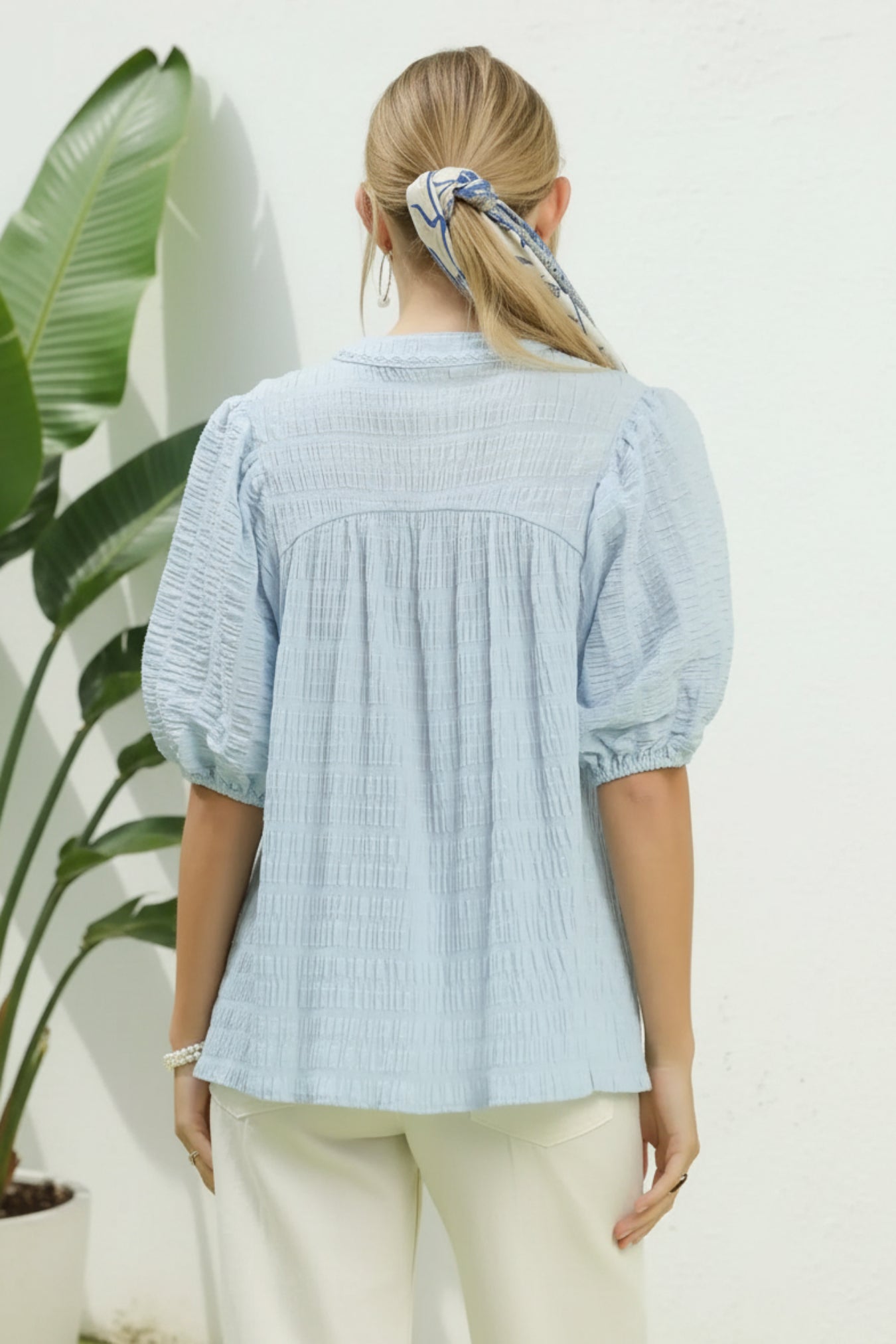 Woman wearing a light blue blouse with puffed sleeves in an indoor setting.