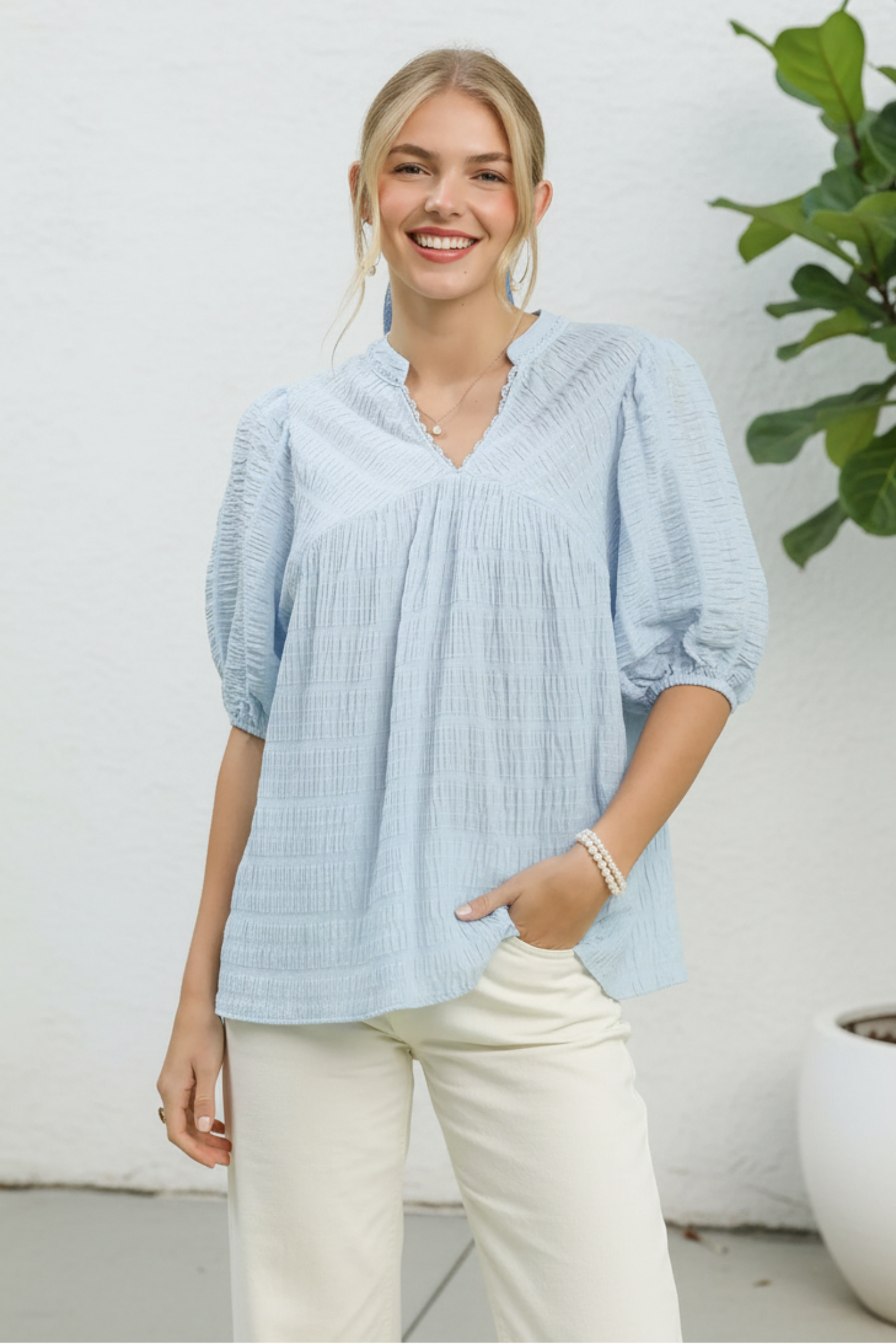 Woman wearing a light blue blouse with a white background and plant