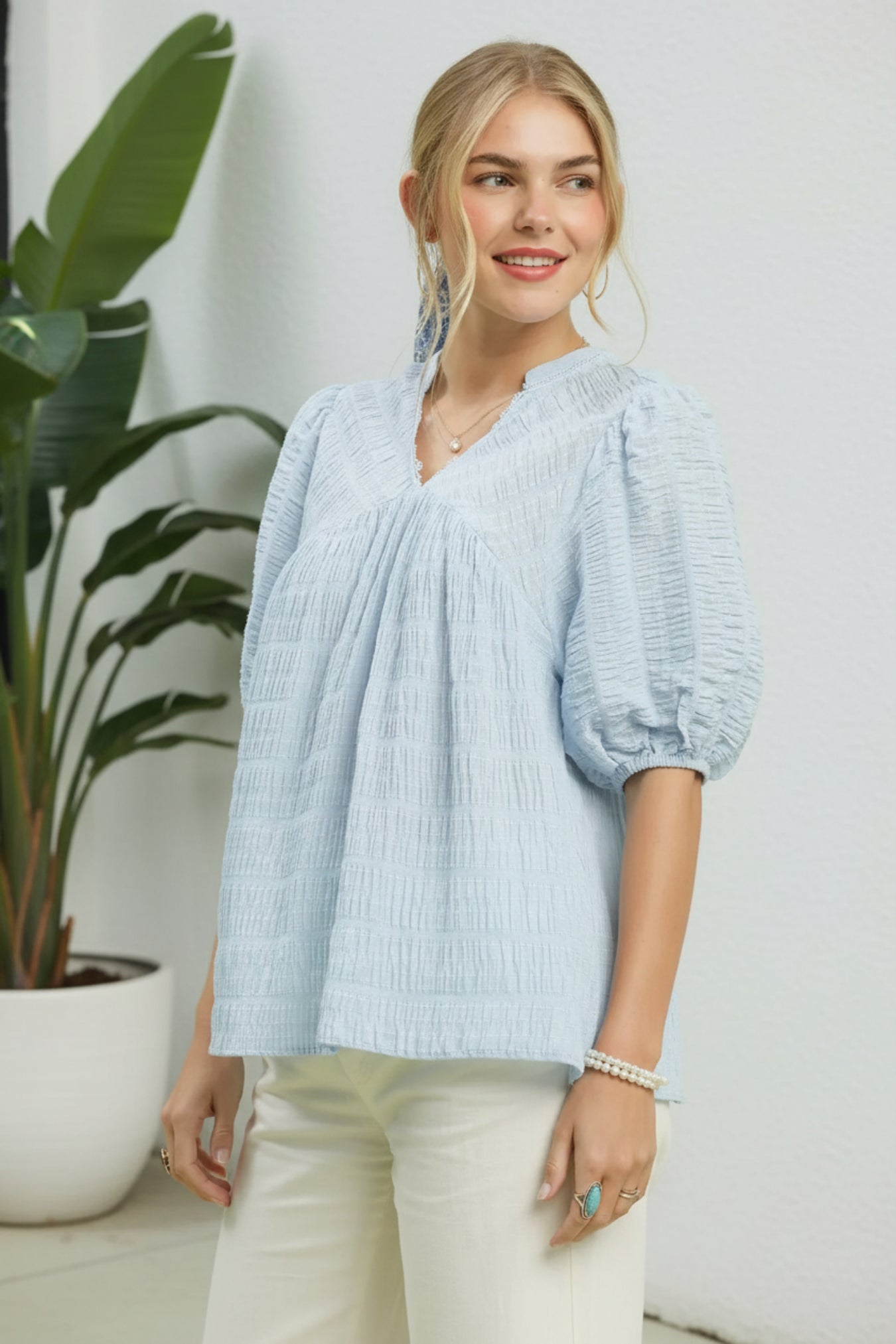 Woman wearing a light blue blouse with puffed sleeves in a home setting.