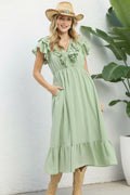 Woman wearing a light green dress with ruffled details, beige boots, and a straw hat on a white background.