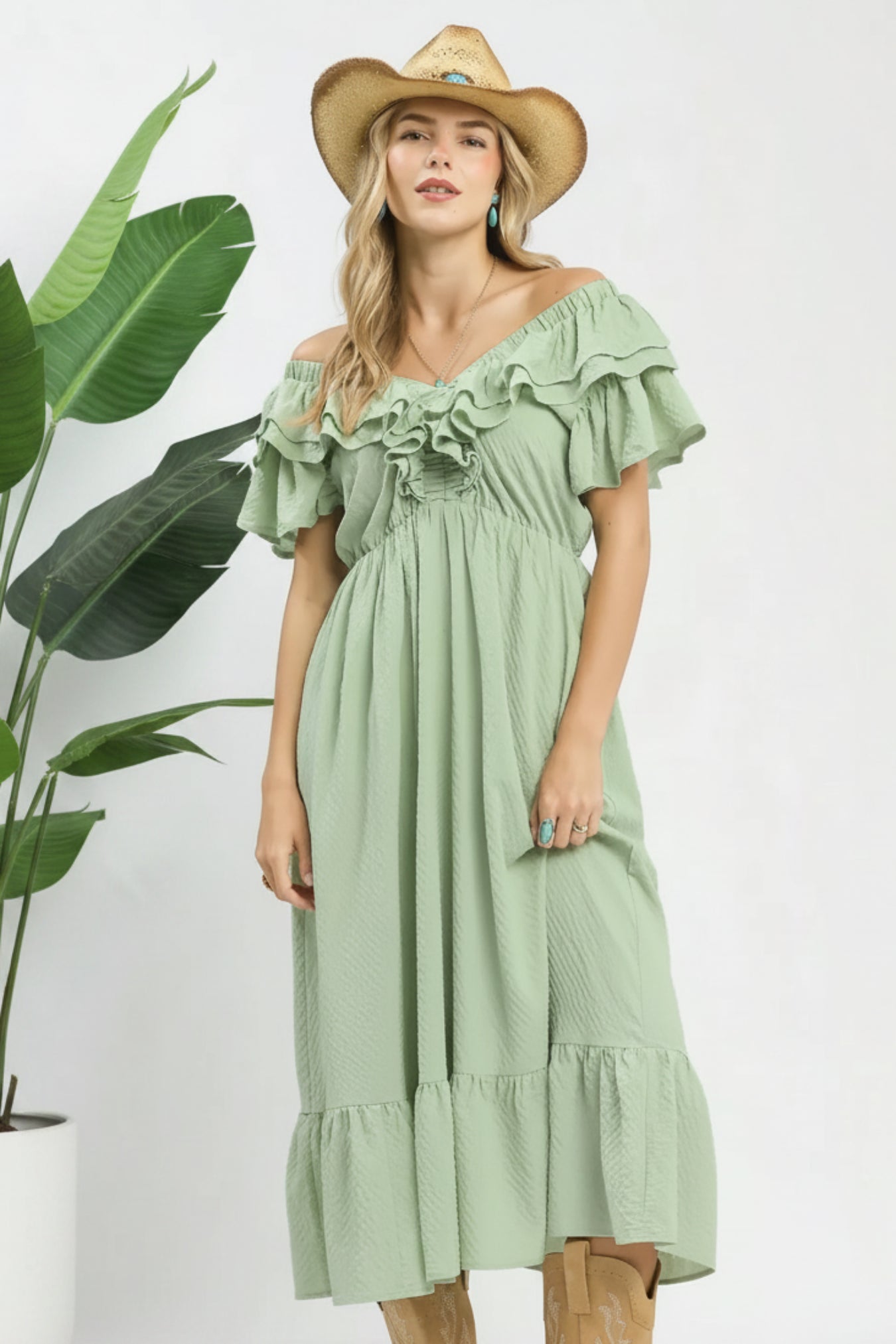 Woman wearing a green dress with ruffled details and a straw hat on a white background