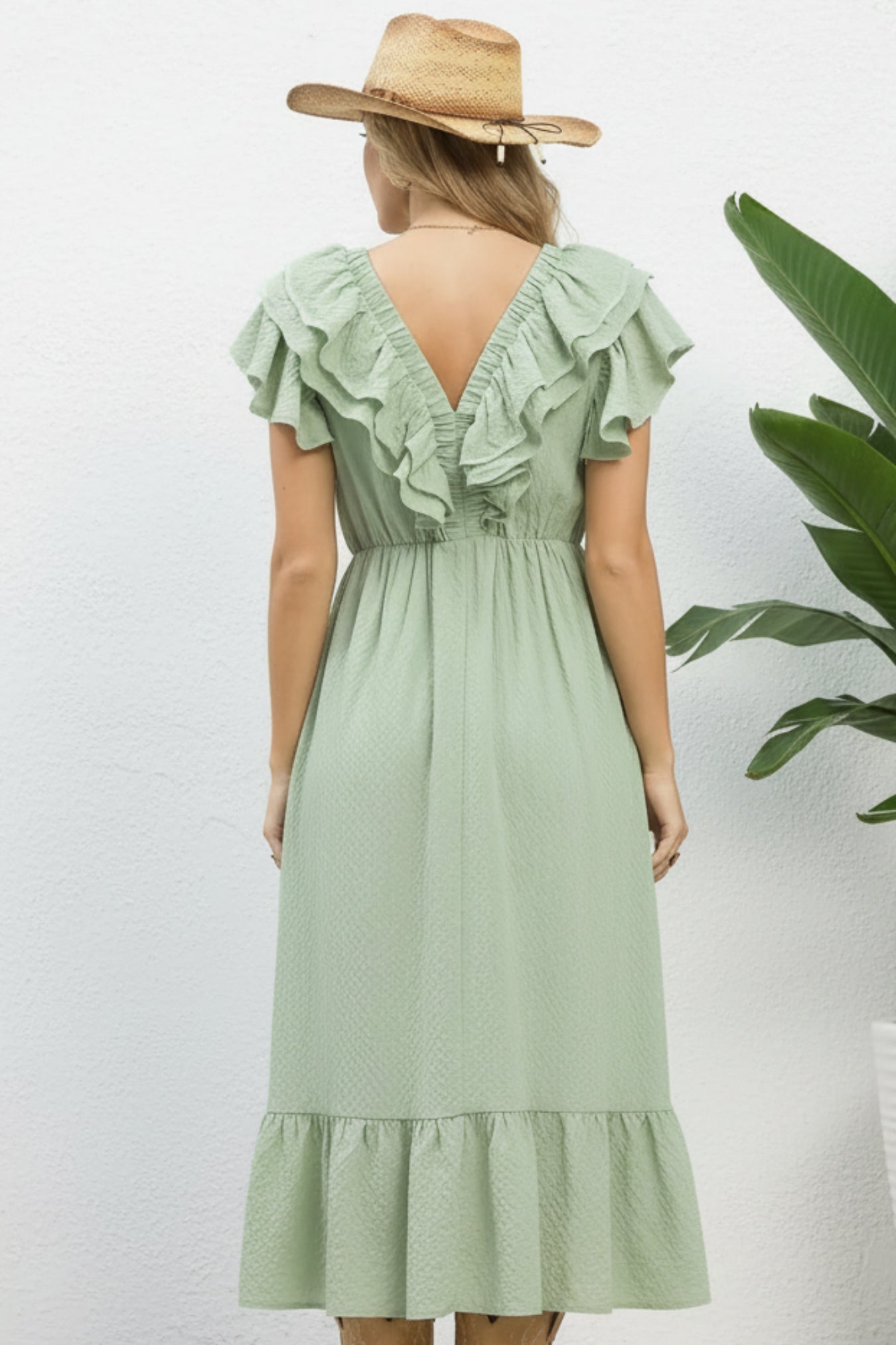Woman wearing a light green dress with ruffled details and a straw hat on a white background.