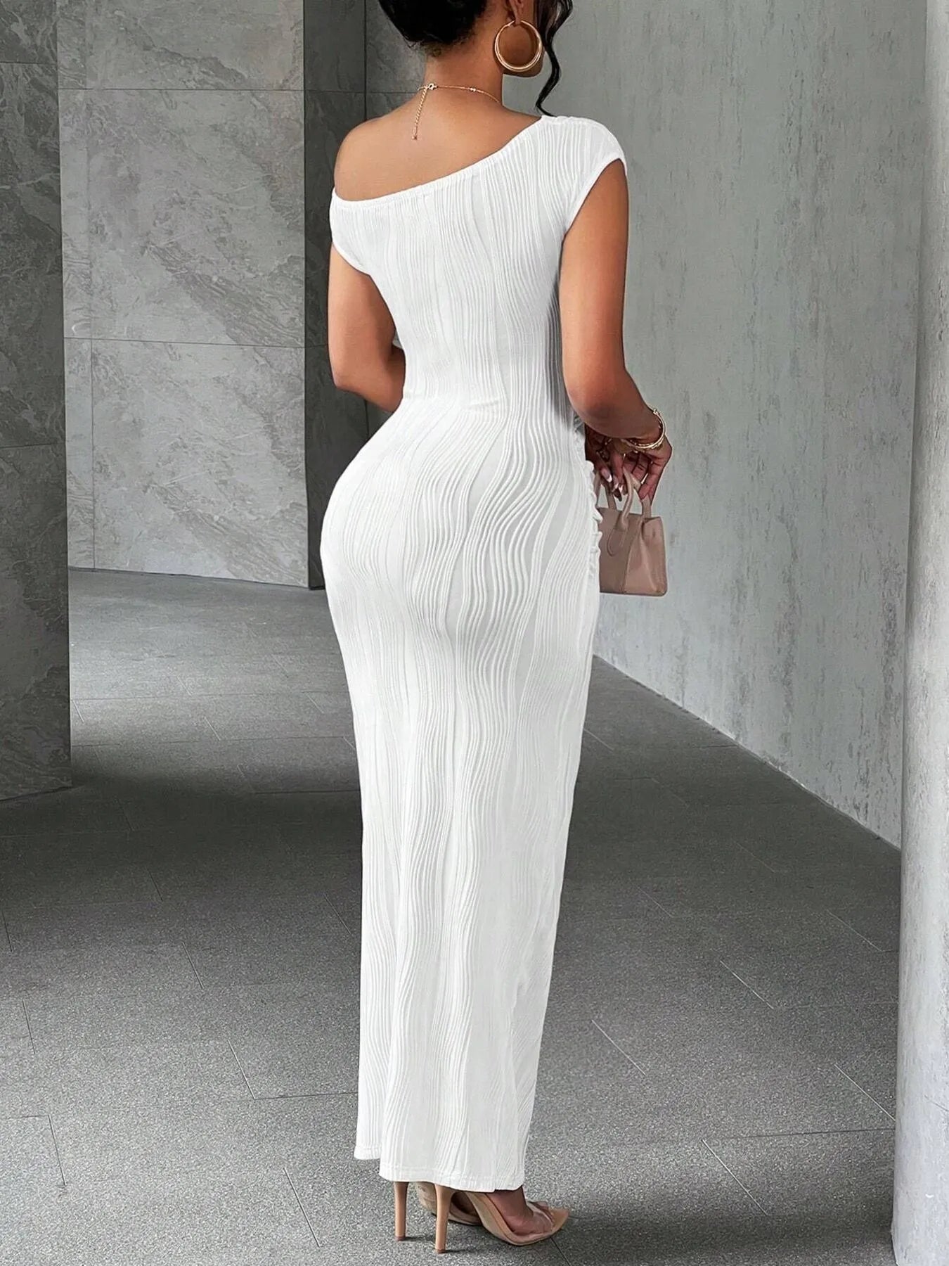 Woman wearing a white one-shoulder dress in a gray room.