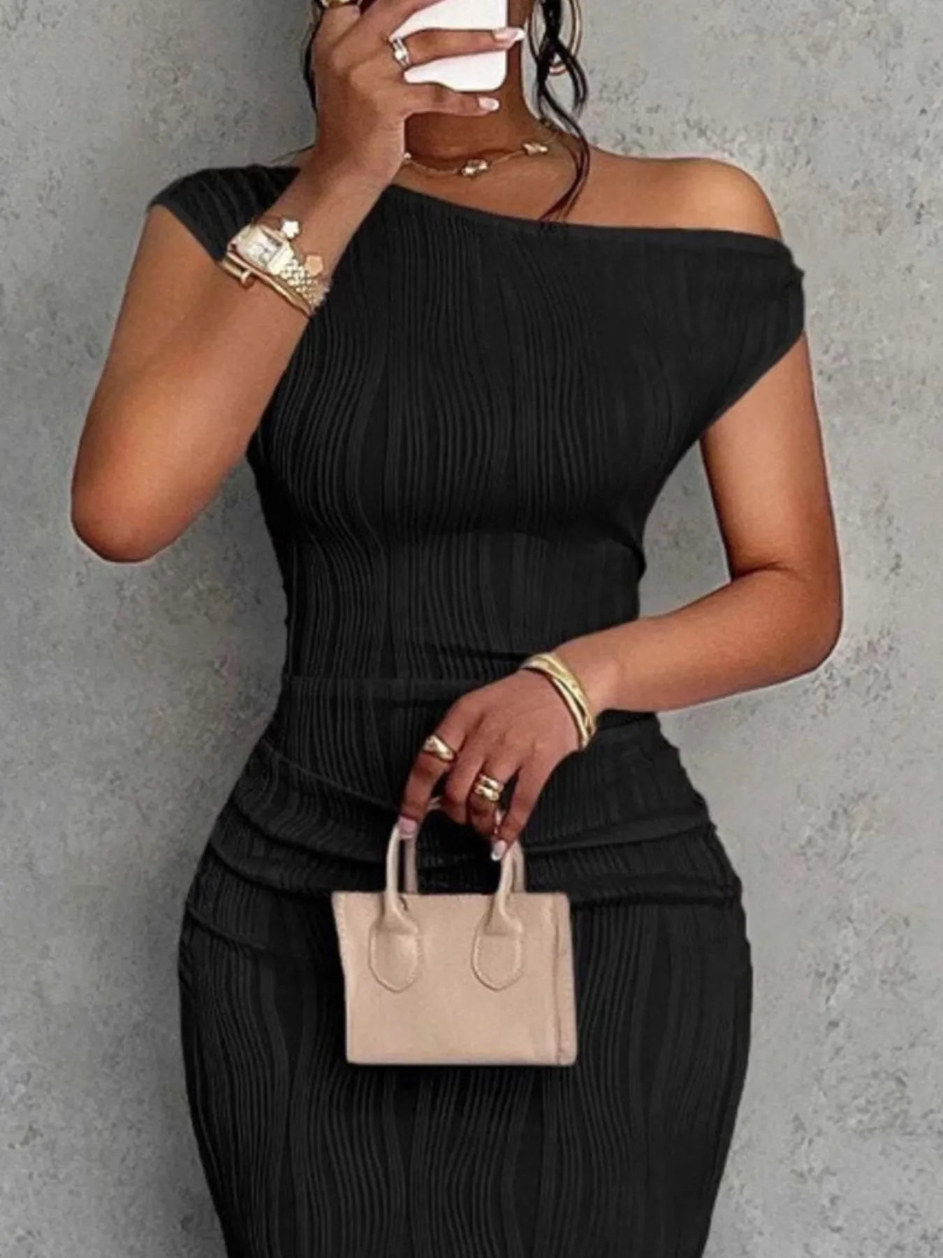Person wearing a black off-shoulder top and skirt with a beige handbag against a gray background