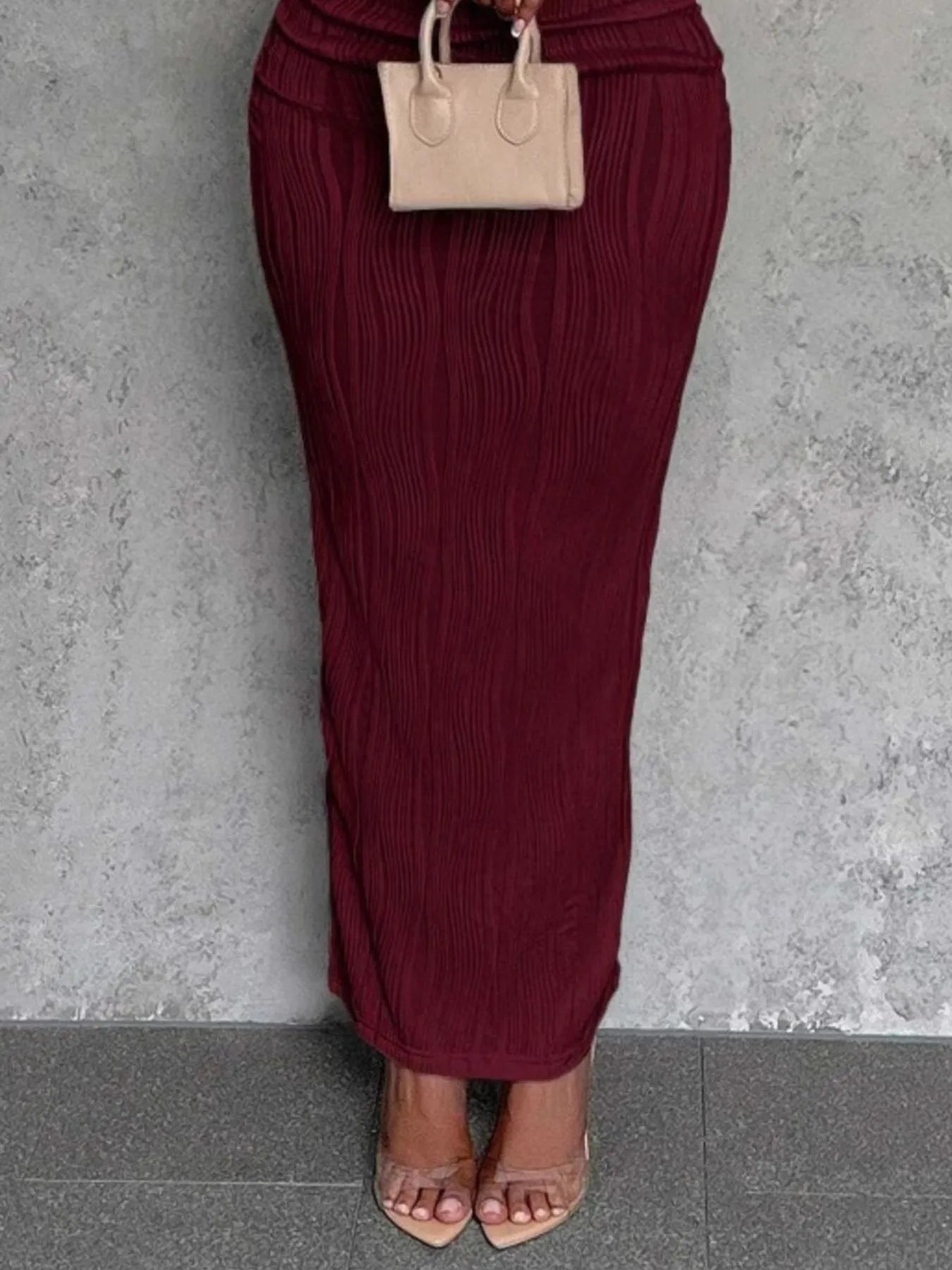 Maroon pleated skirt with beige handbag against a gray wall
