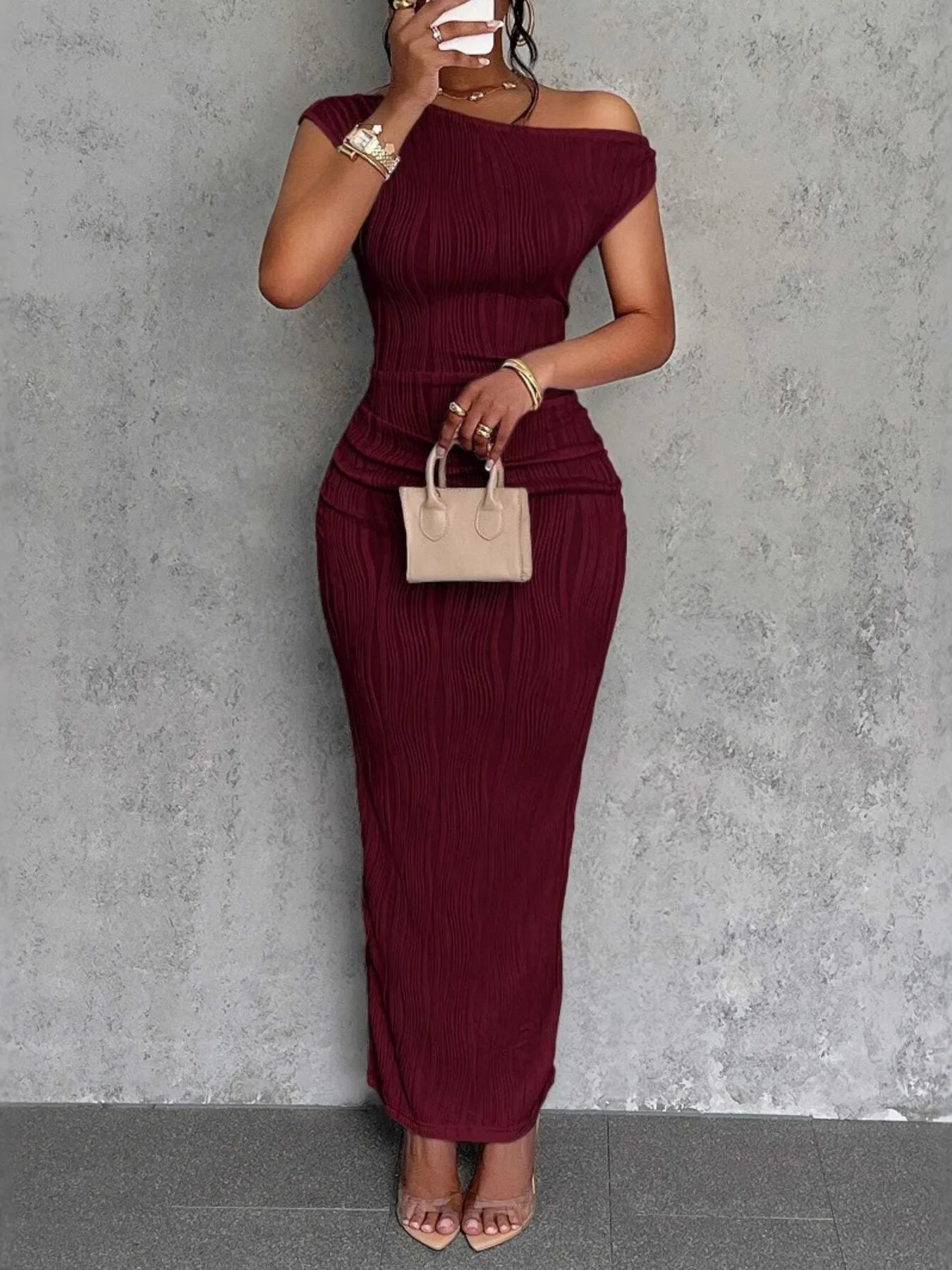 Woman wearing a burgundy off-shoulder dress against a gray wall.