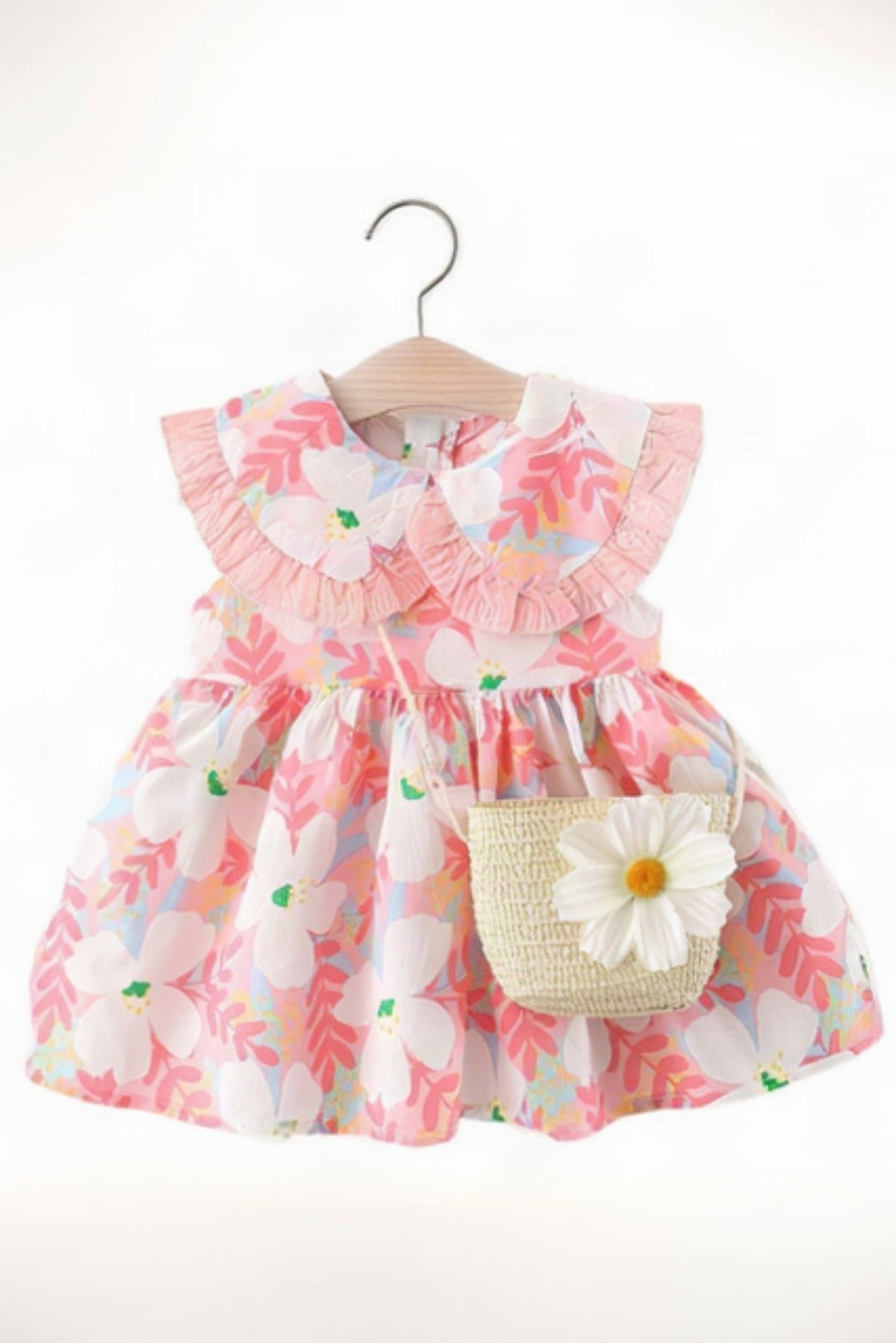 A toddler girl's sleeveless dress with a pink and white floral print, featuring a ruffled Peter Pan collar and a built-in straw bag with a white flower accent, hanging on a wooden hanger against a white background.