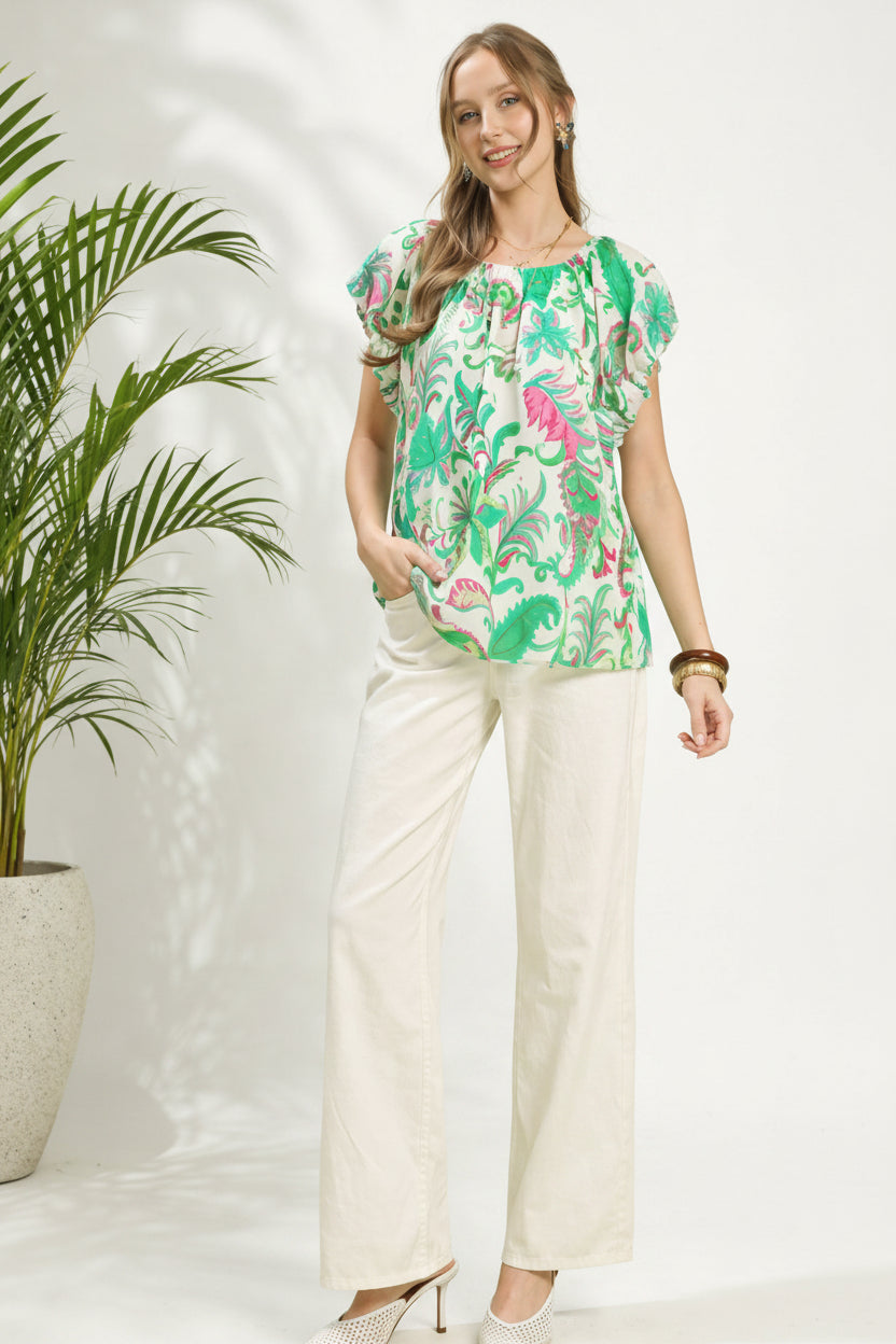 Woman wearing a colorful floral blouse and white pants against a green background