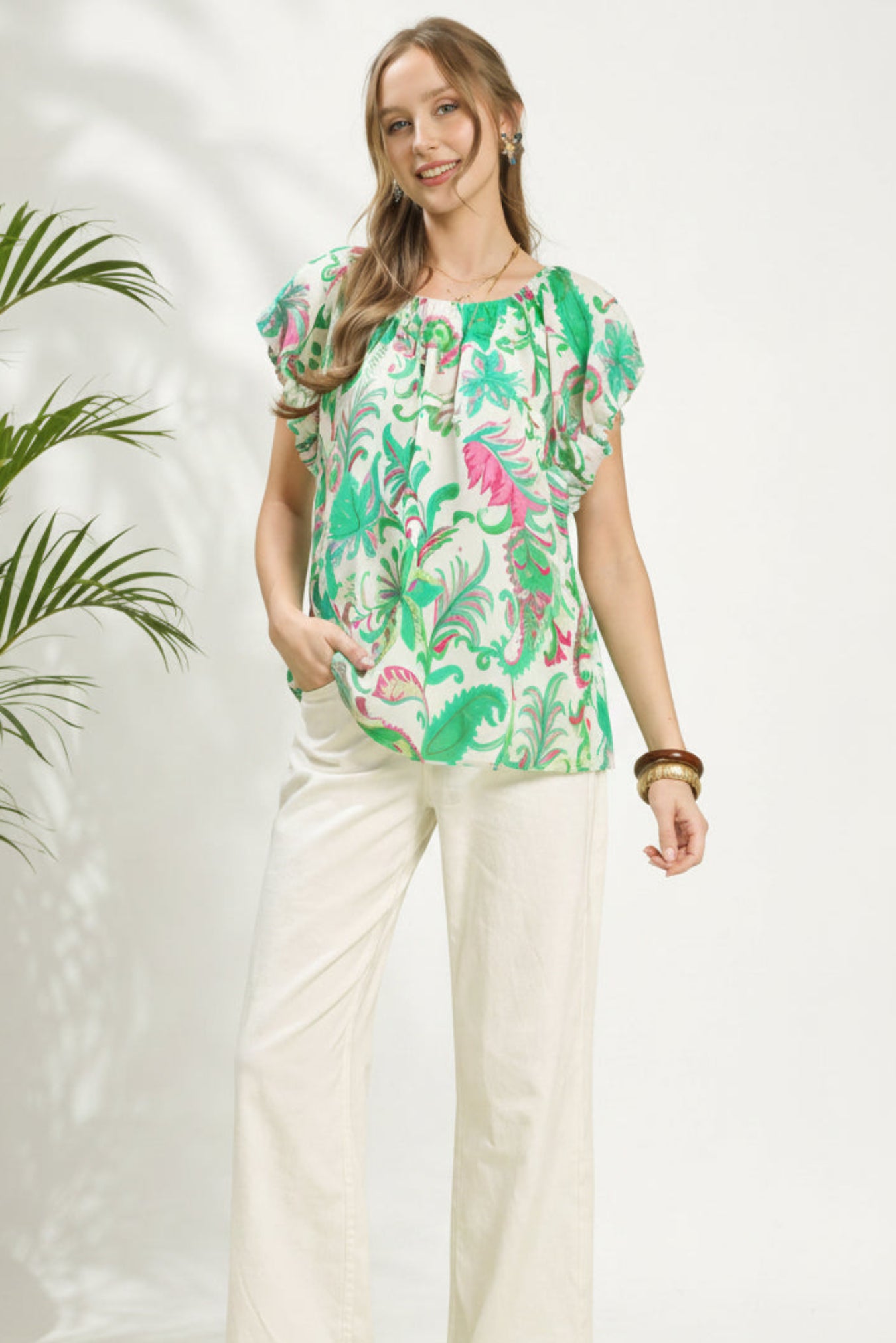 Woman wearing a colorful floral blouse and white pants against a white Background