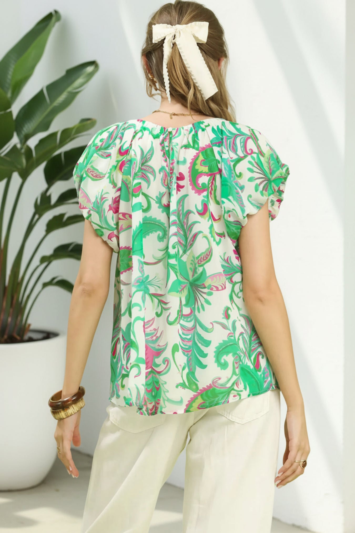 Woman wearing a colorful patterned blouse with a plant in the background