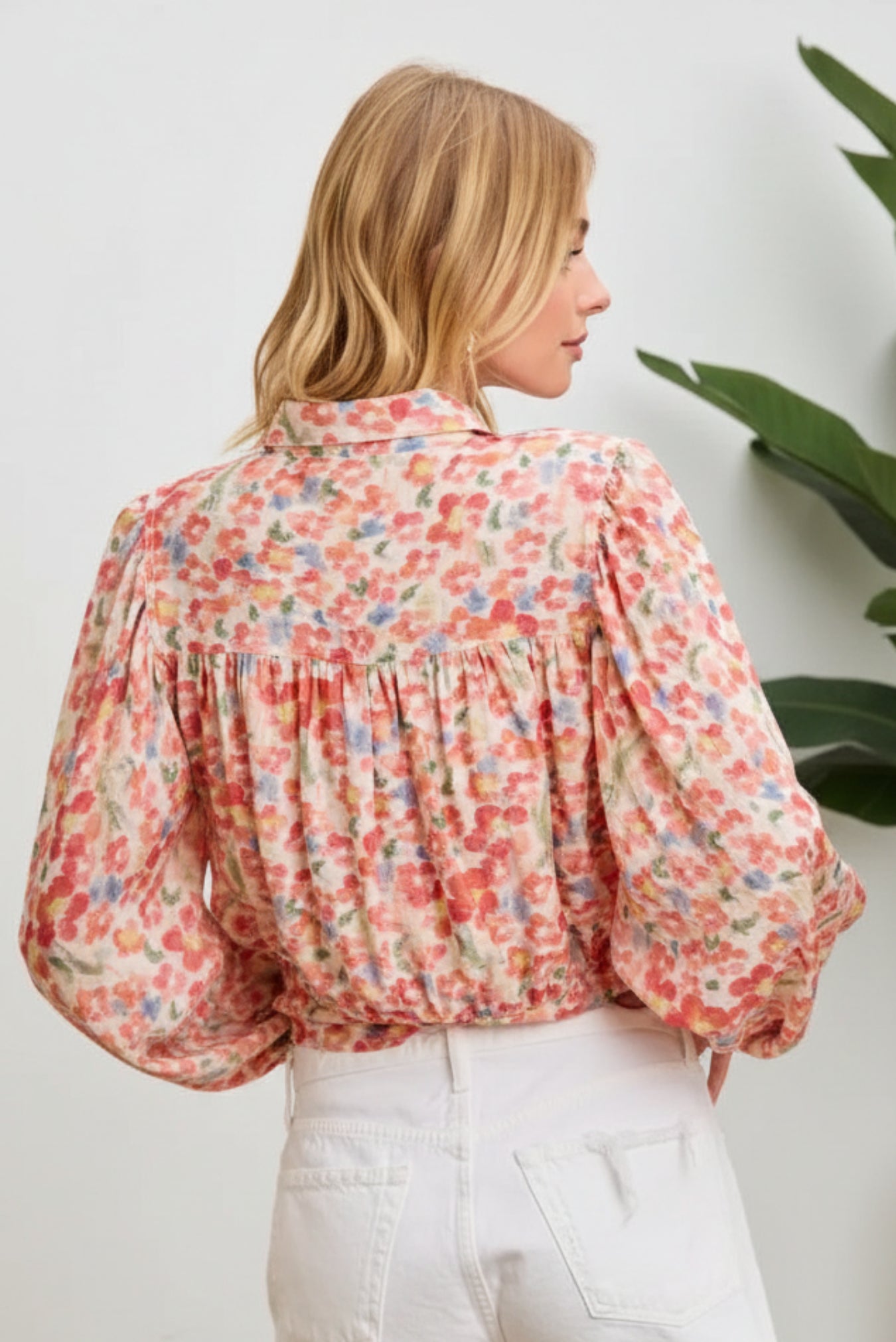 Woman wearing a floral blouse and white shorts against a pink background