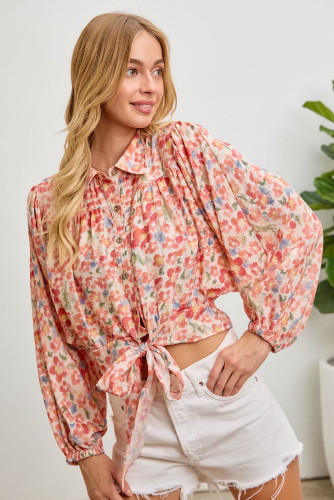 Woman wearing a floral blouse and white shorts on a pink background