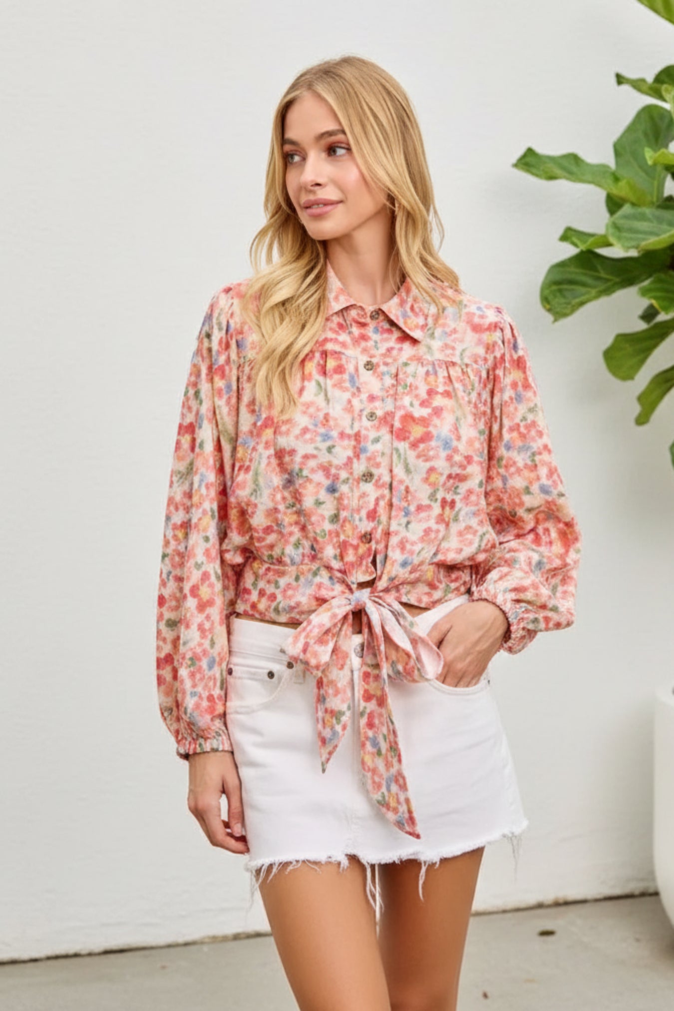Woman wearing a floral blouse with a tie waist on a pink background