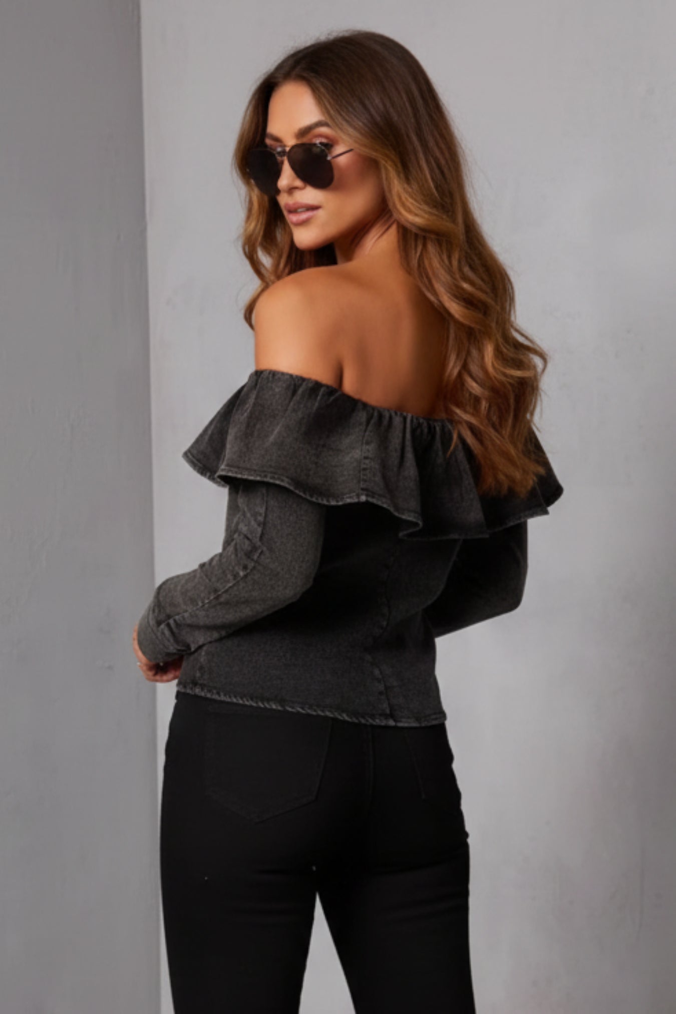 Woman wearing a black off-shoulder top against a gray background