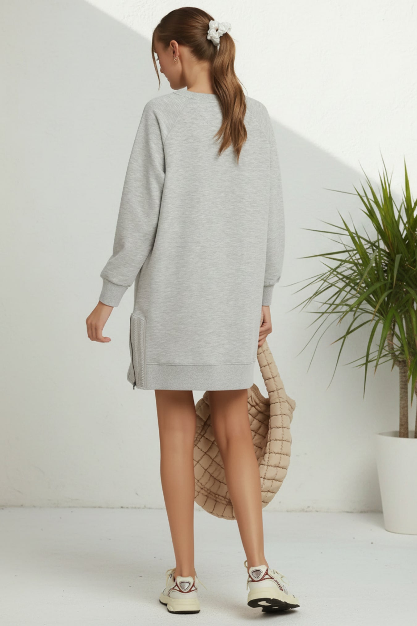 Person wearing a gray dress holding a beige bag on a plain background