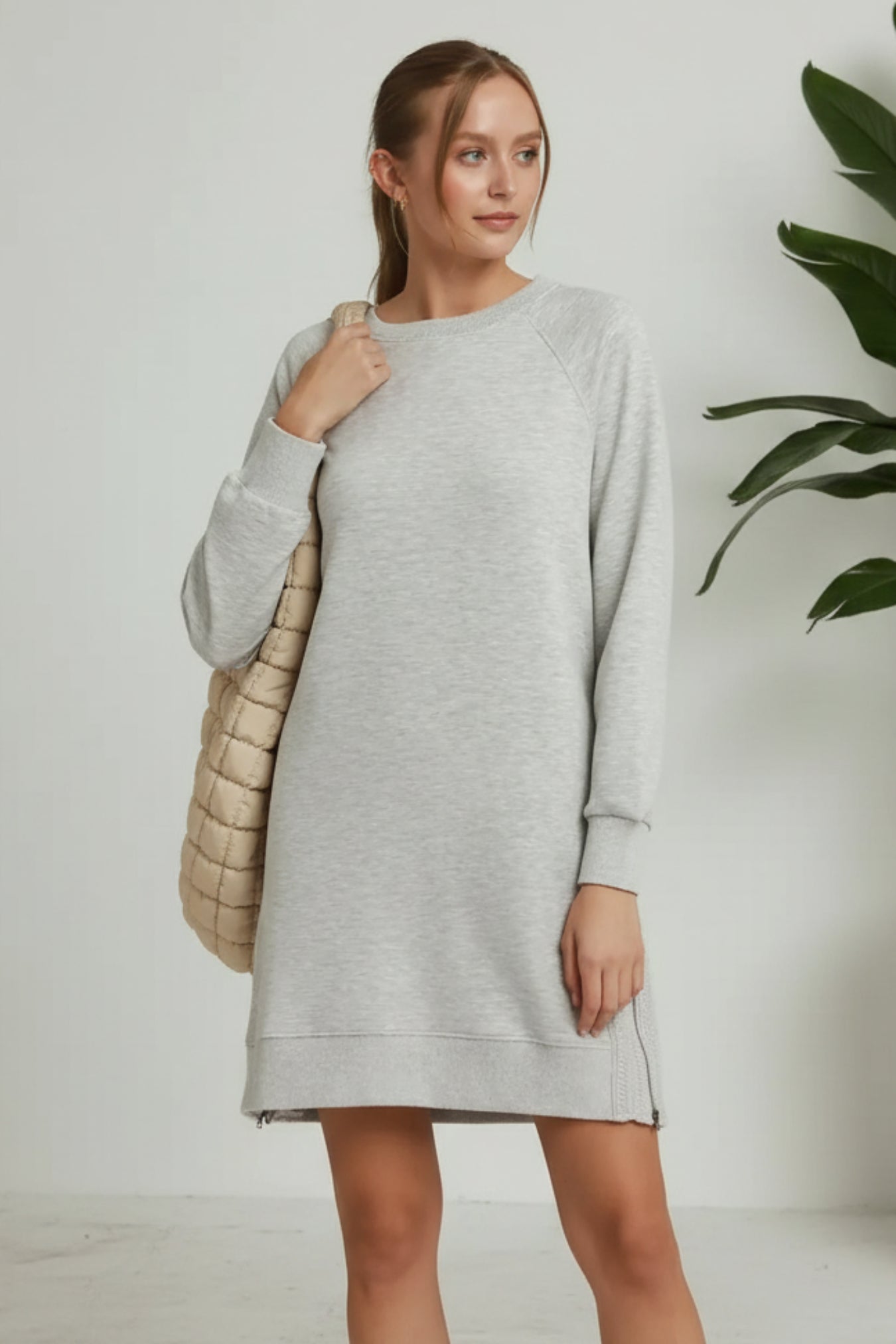 Woman wearing a gray dress with a beige quilted bag on a plain background