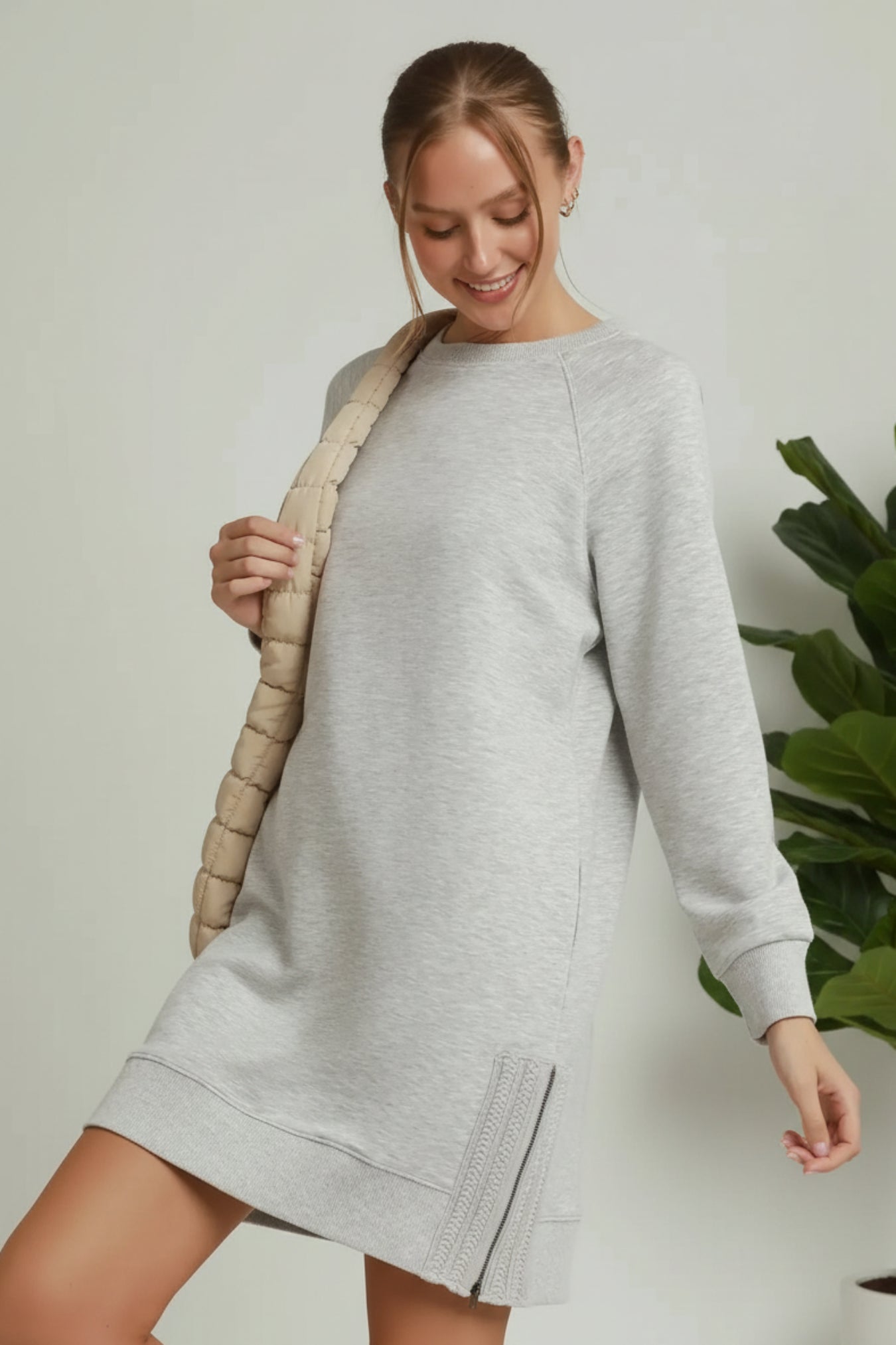 Woman wearing a gray sweatshirt dress with a beige jacket over it on a light background