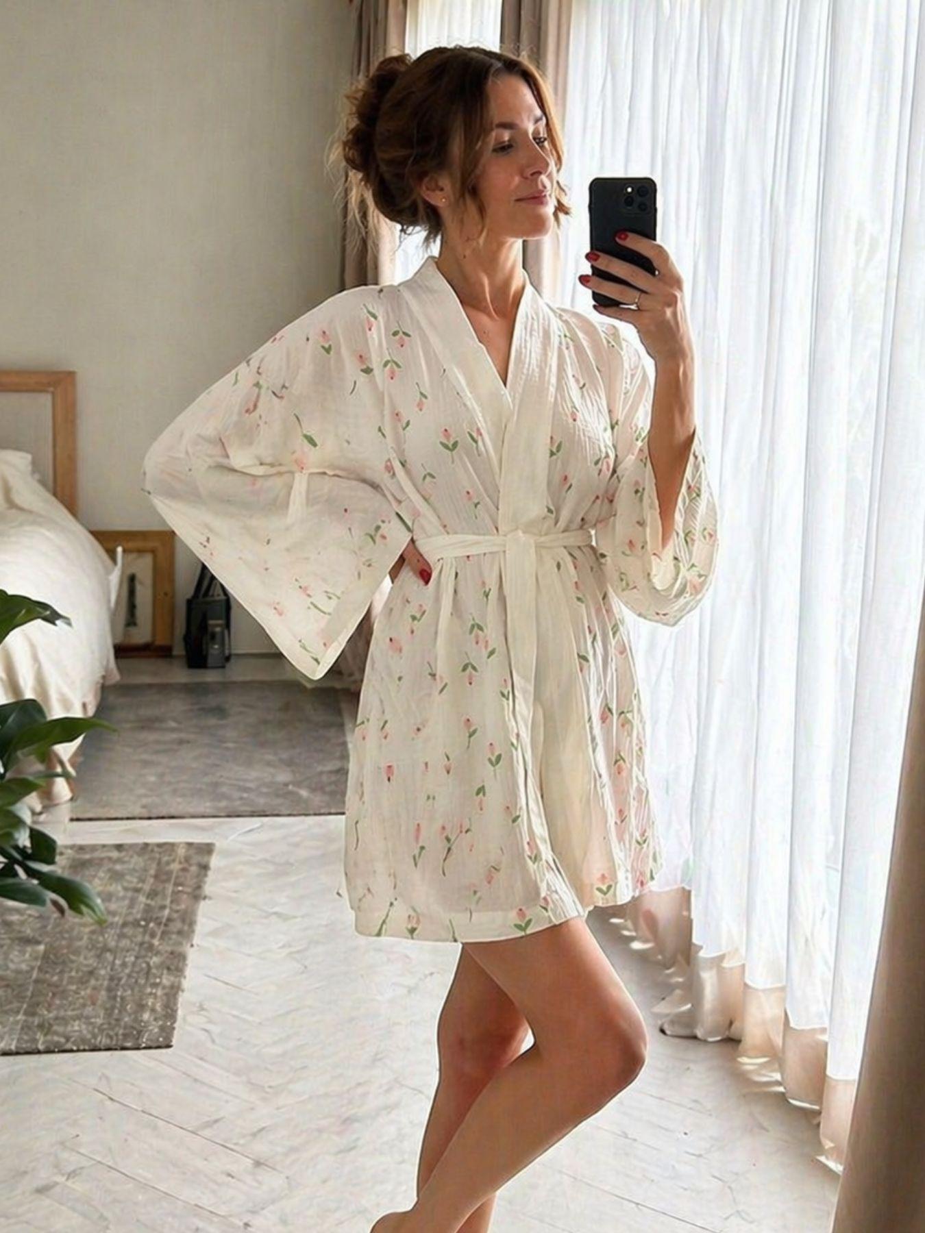 Woman in a floral robe taking a mirror selfie in a bright room.