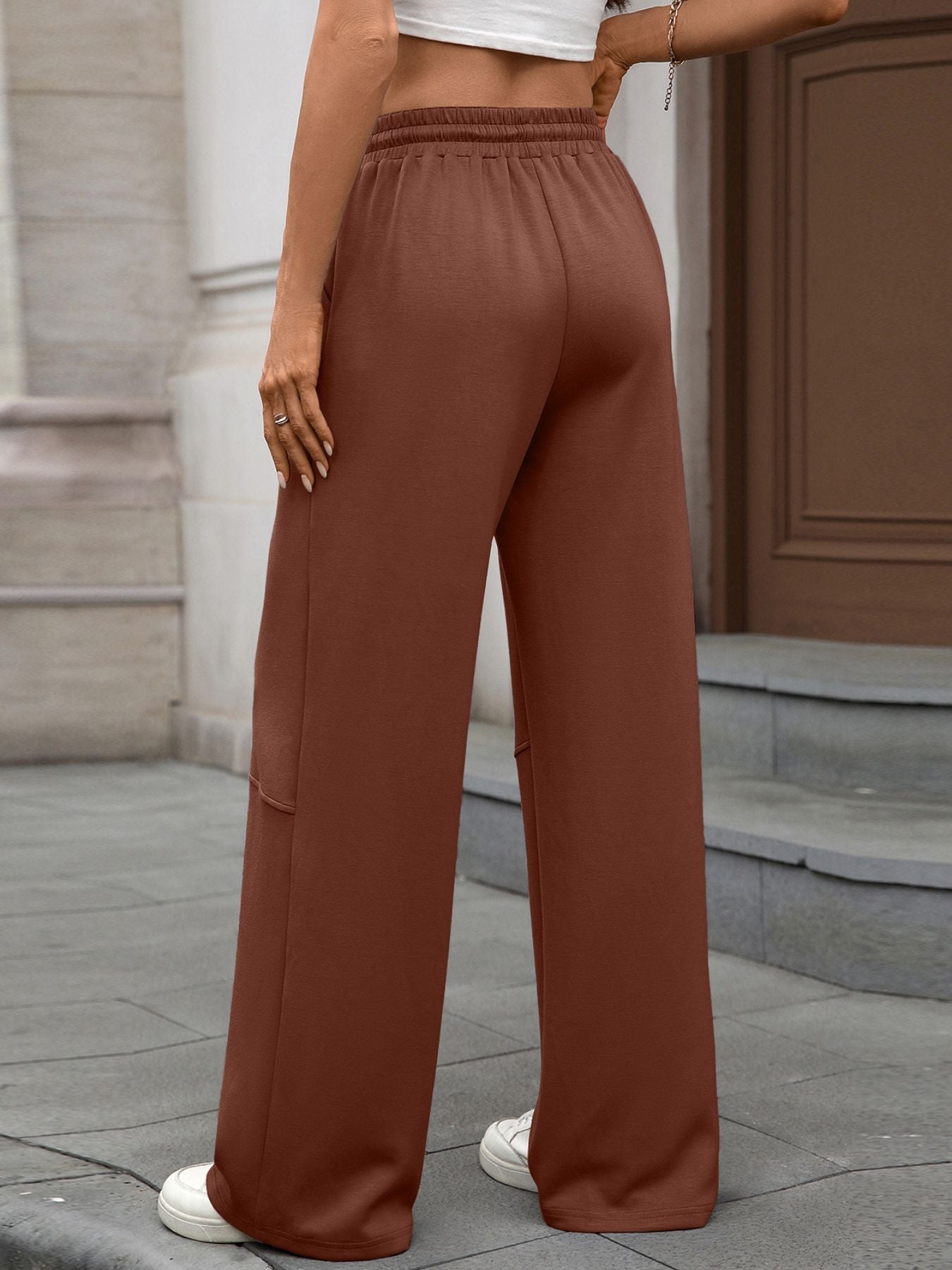 Person wearing brown wide-leg pants standing on a sidewalk.