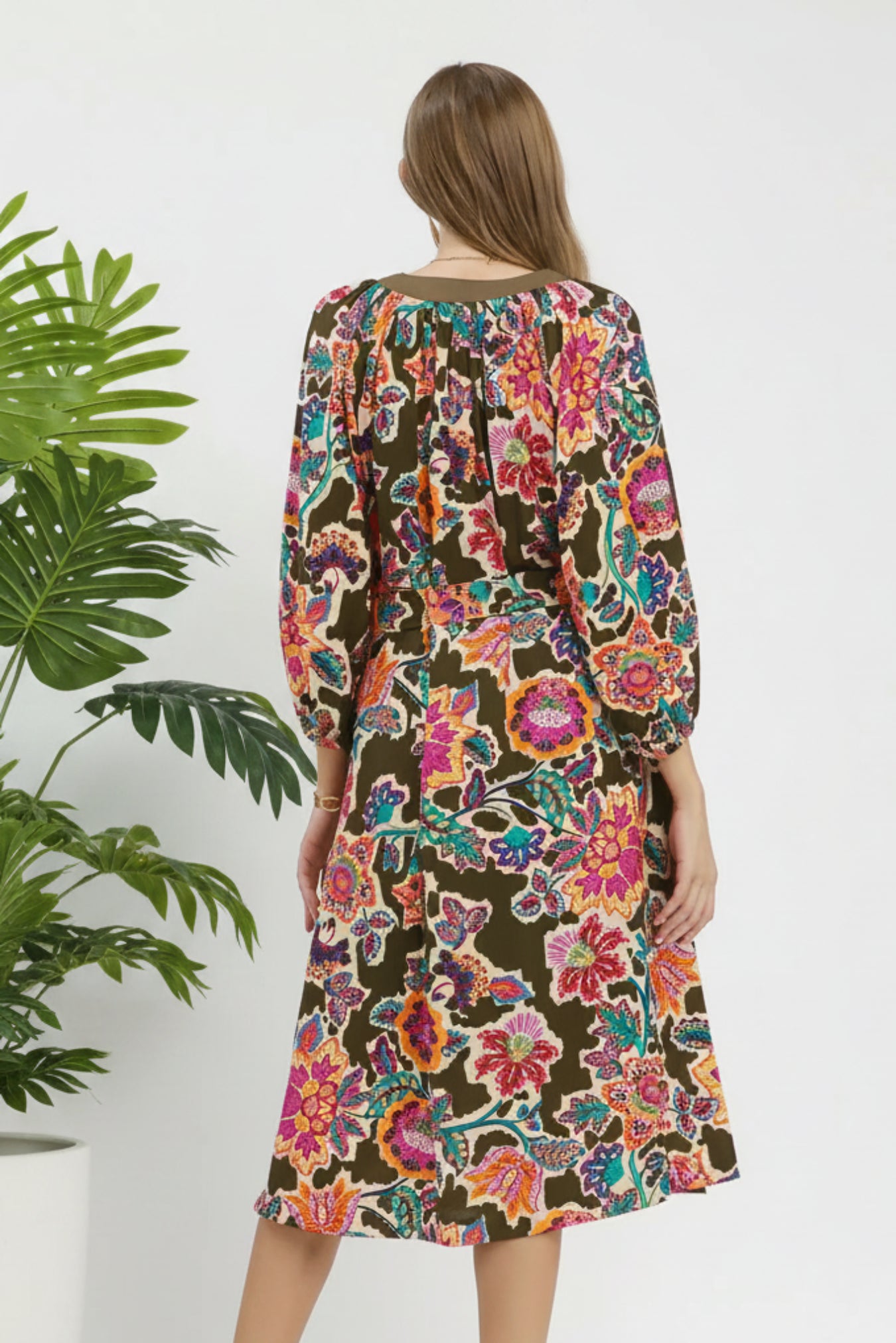 Woman wearing a colorful floral dress on a white background next to a plant
