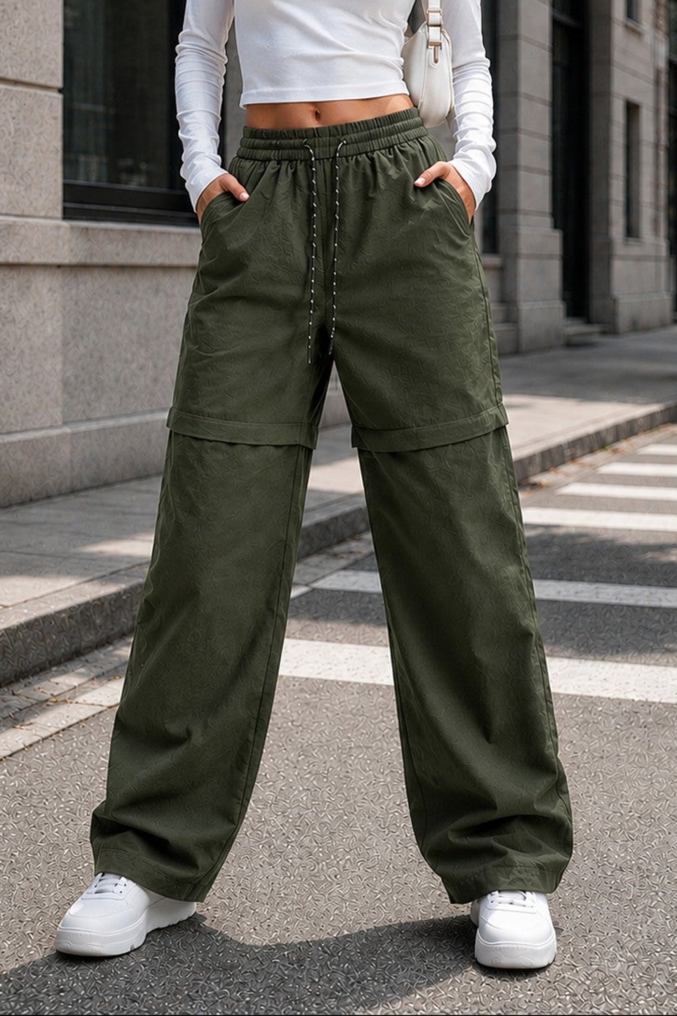 A woman stands on a city street wearing olive green wide-leg cargo pants, a white long-sleeve crop top, and white sneakers.