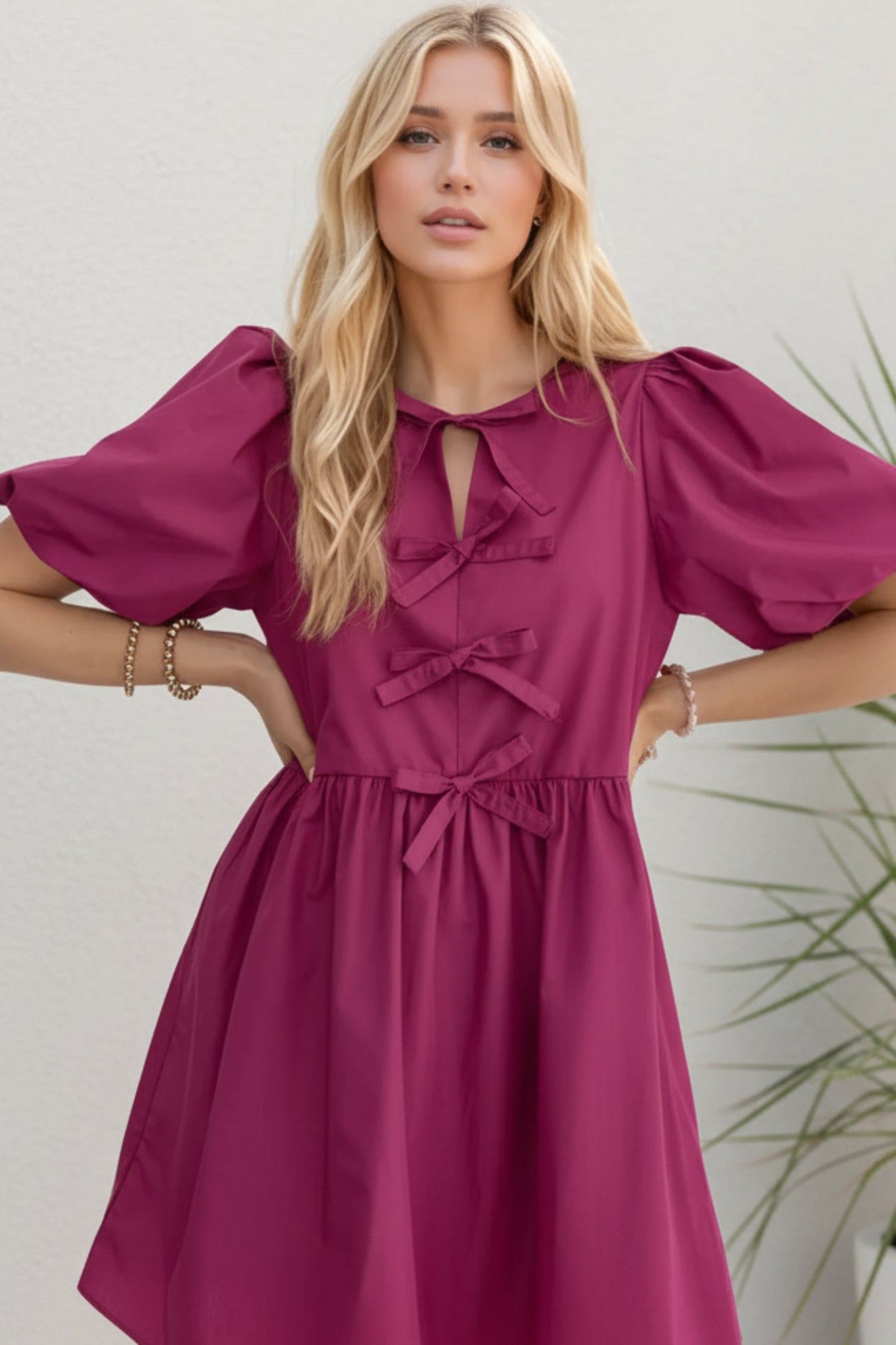 Woman wearing a magenta dress with puff sleeves on a light background