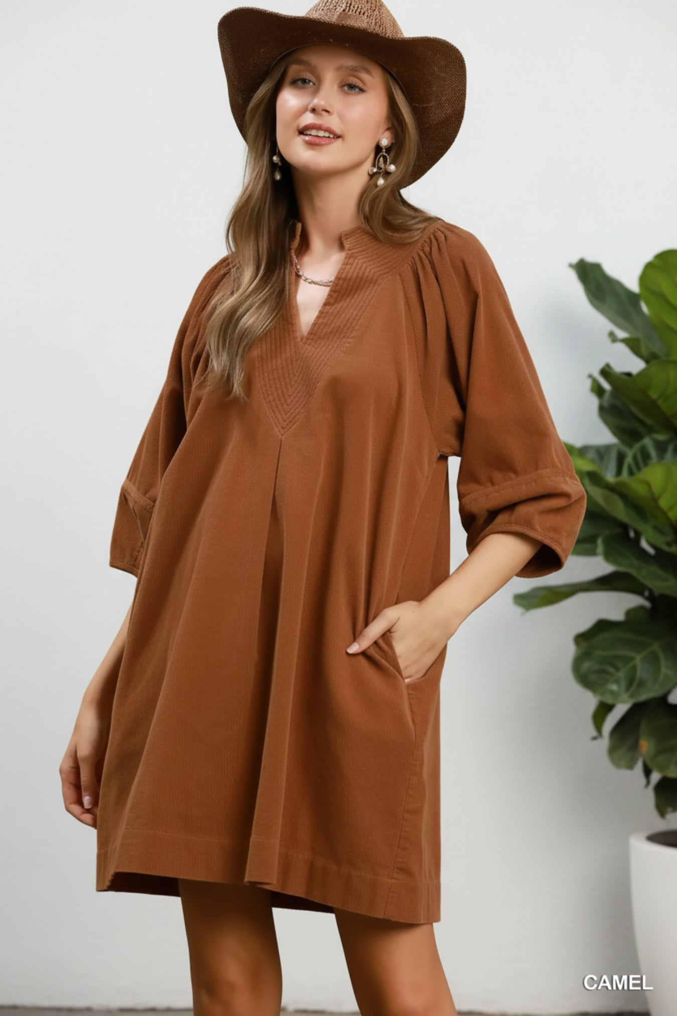 A woman wearing a camel brown linen-blend tunic dress with three-quarter sleeves and a matching wide-brim hat, posed against a white background.
