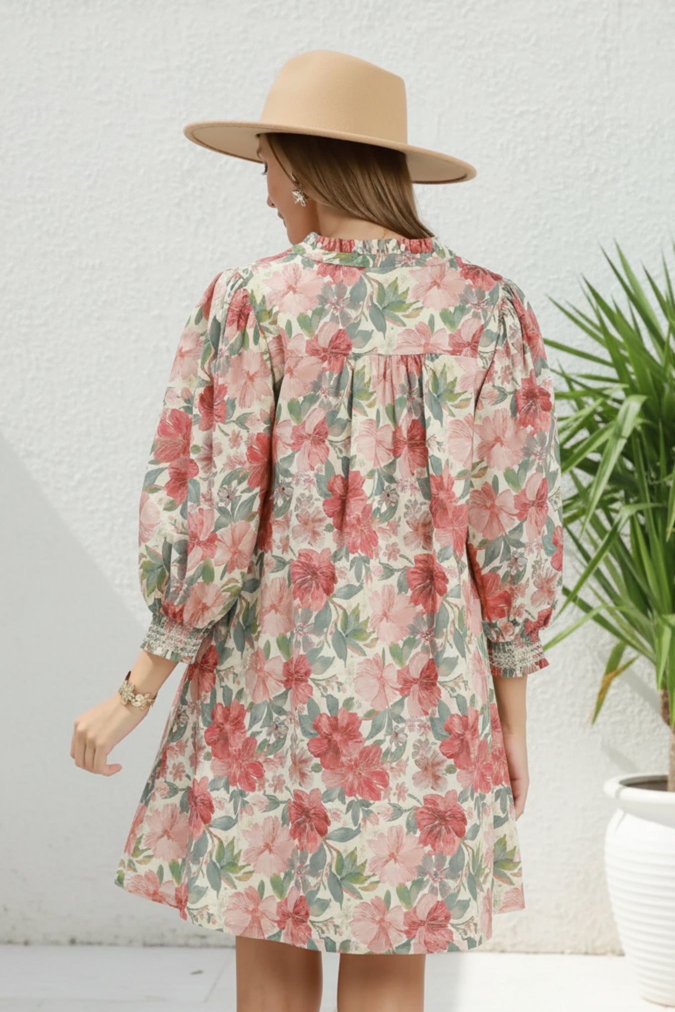Woman wearing a floral dress with long sleeves and a hat on a plain background