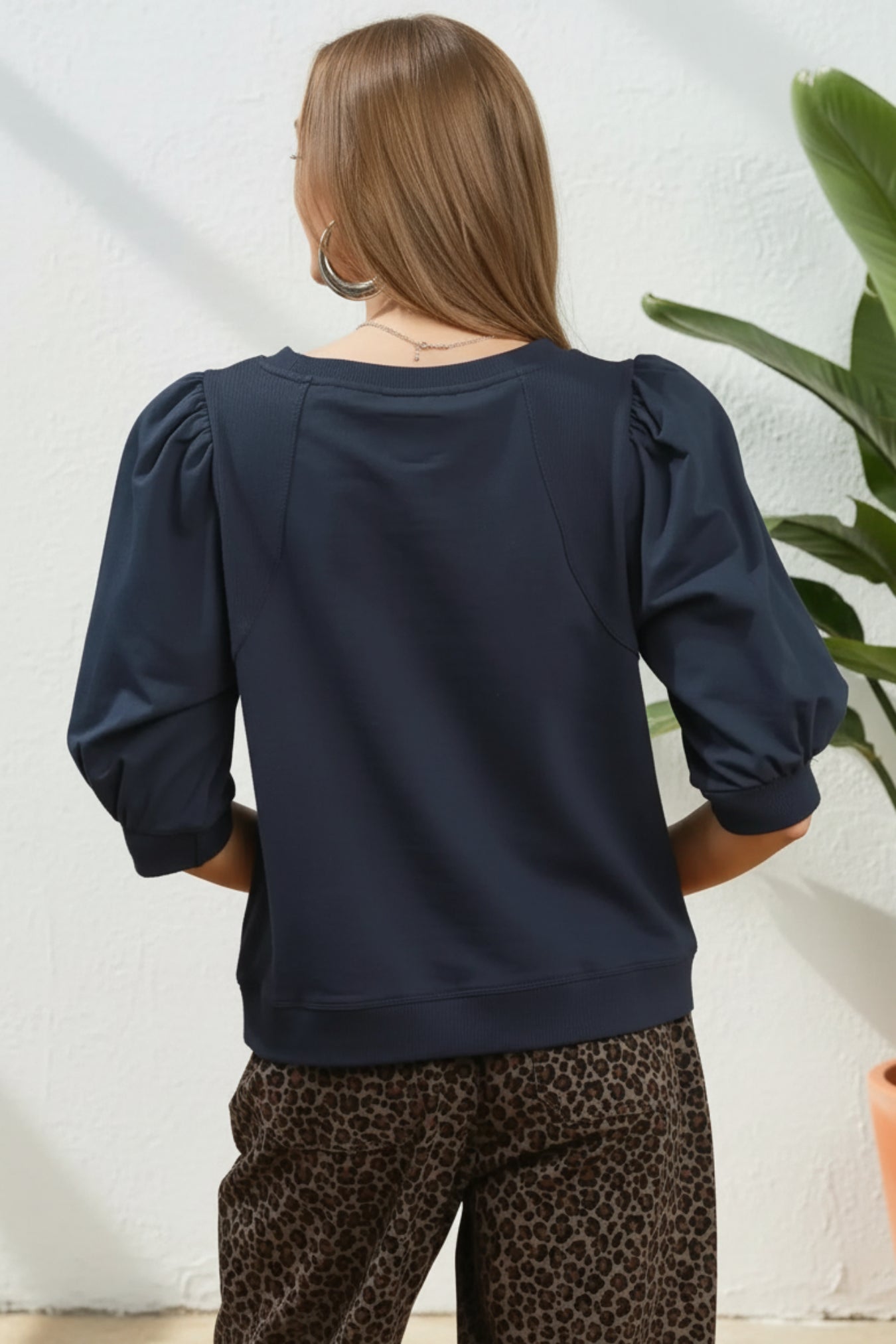 Woman wearing a navy blue top with puffed sleeves against a white background