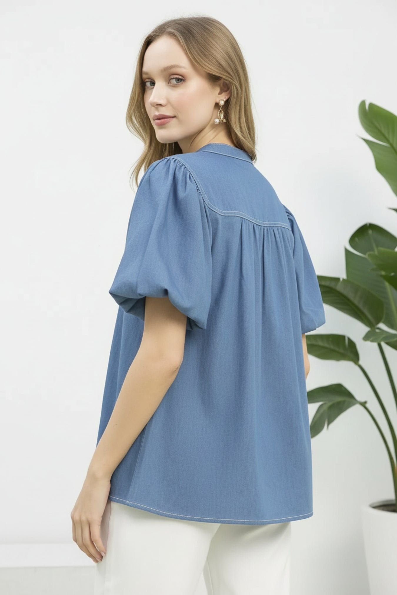 Woman wearing a light denim blouse with puff sleeves on a light green background