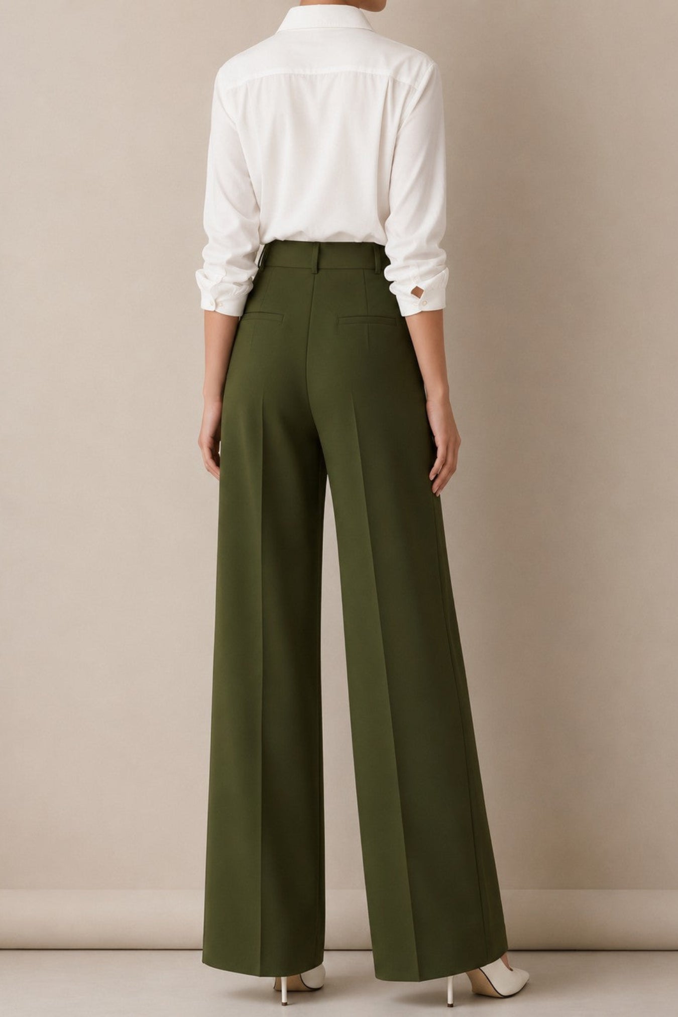 A model shown from the back wearing high-waisted olive green wide-leg trousers, a white button-down shirt, and white heels against a neutral beige studio background.