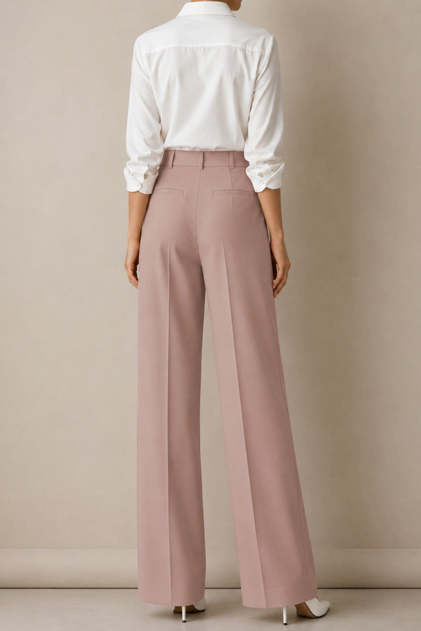 A model shown from the back wearing dusty pink wide-leg trousers, a white long-sleeve button-up shirt, and white heels, set against a neutral beige studio background.