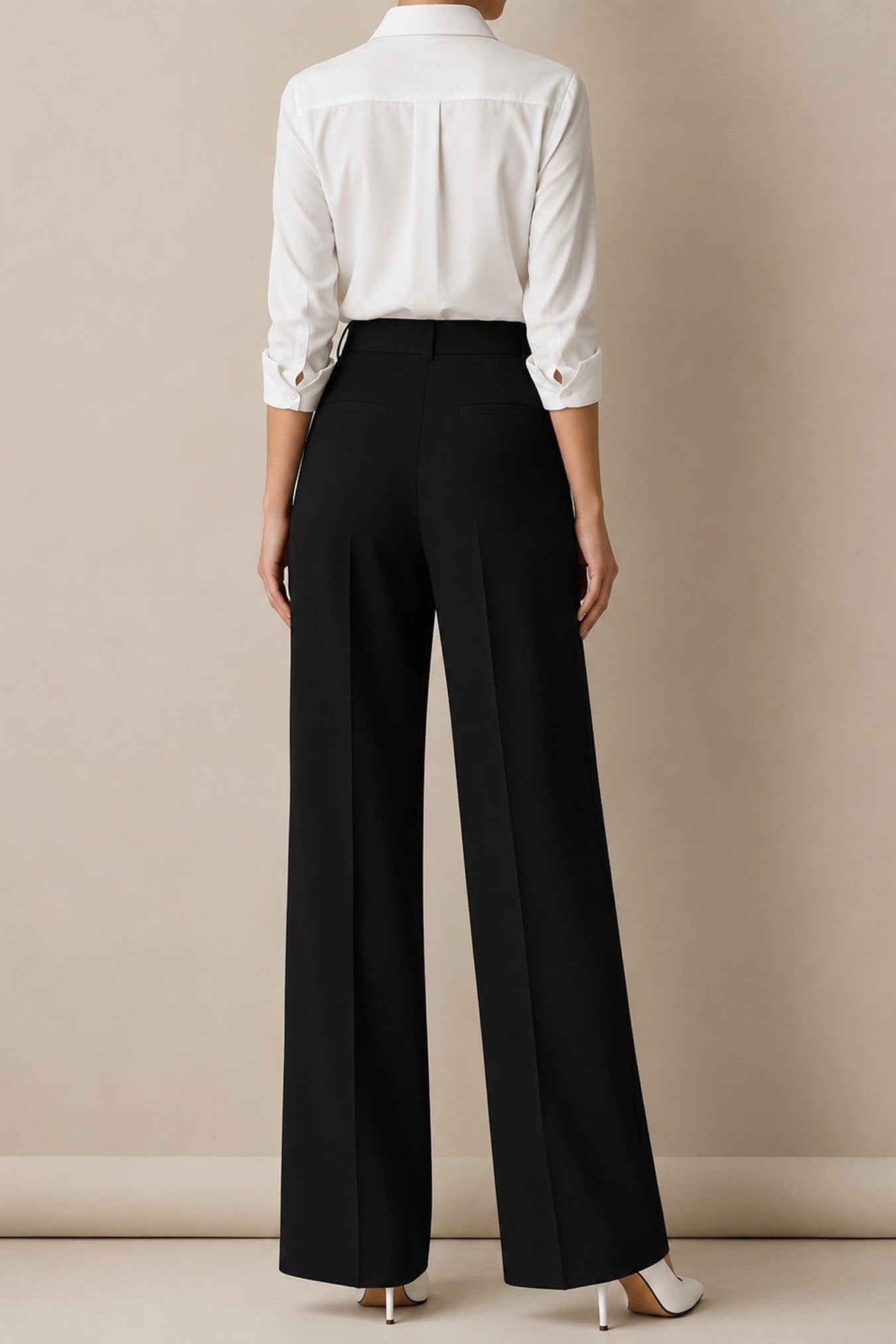 A model shown from the back wearing a white long-sleeve button-down shirt and black wide-leg trousers, paired with white high-heeled shoes, against a neutral beige studio background.
