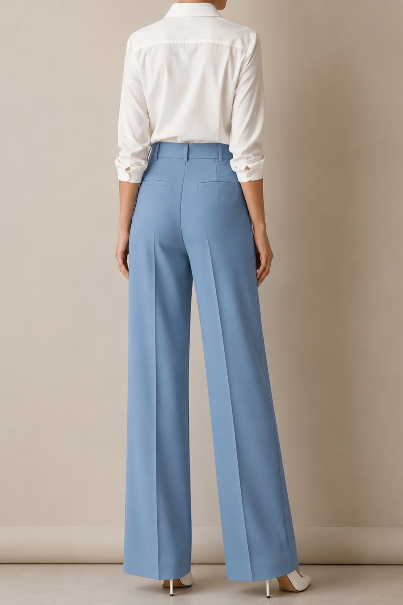 A model shown from the back wearing light blue wide-leg trousers and a white button-down shirt, standing against a neutral beige studio wall.