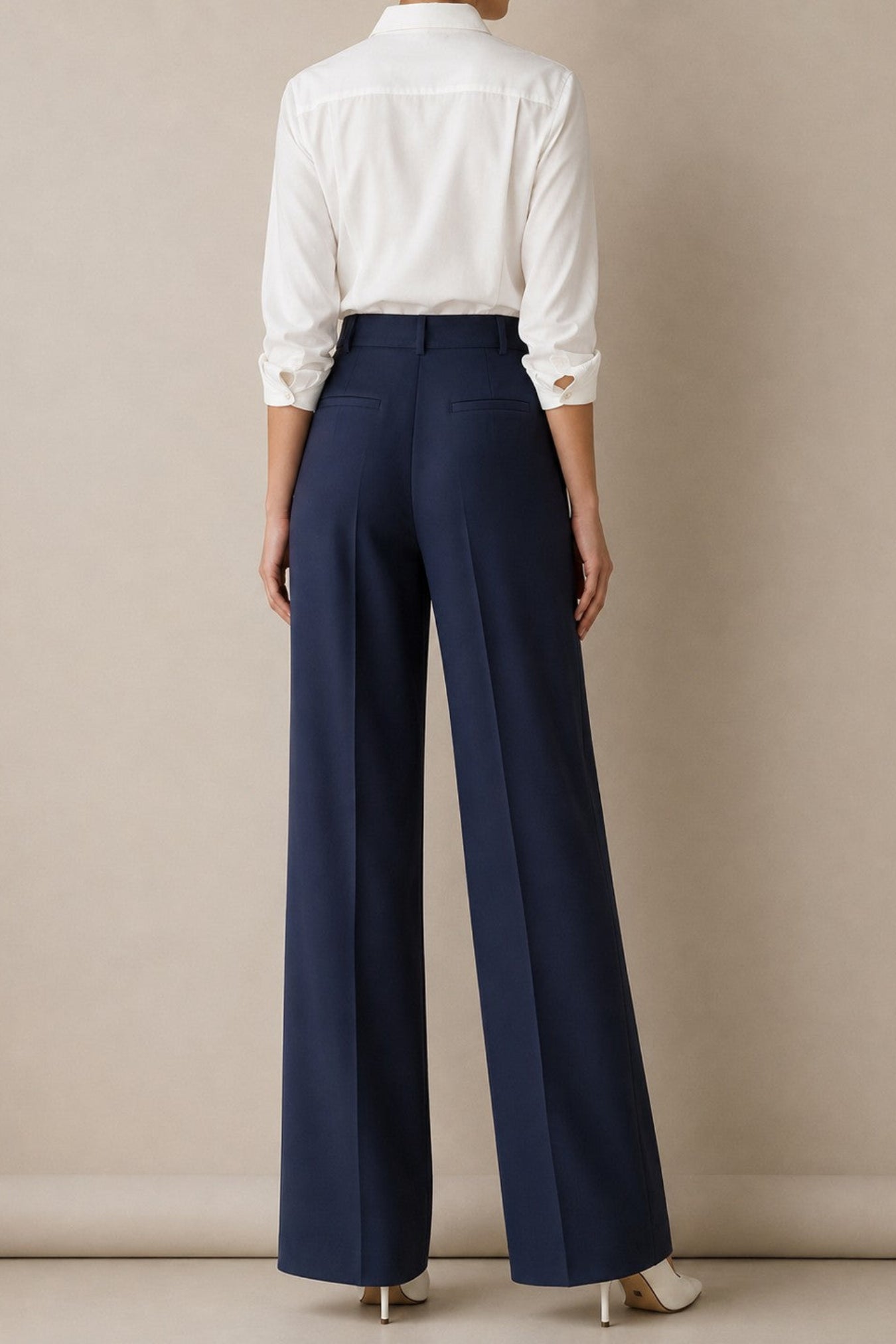 A model shown from the back wearing navy blue wide-leg trousers and a white button-down shirt, standing against a neutral beige studio background.
