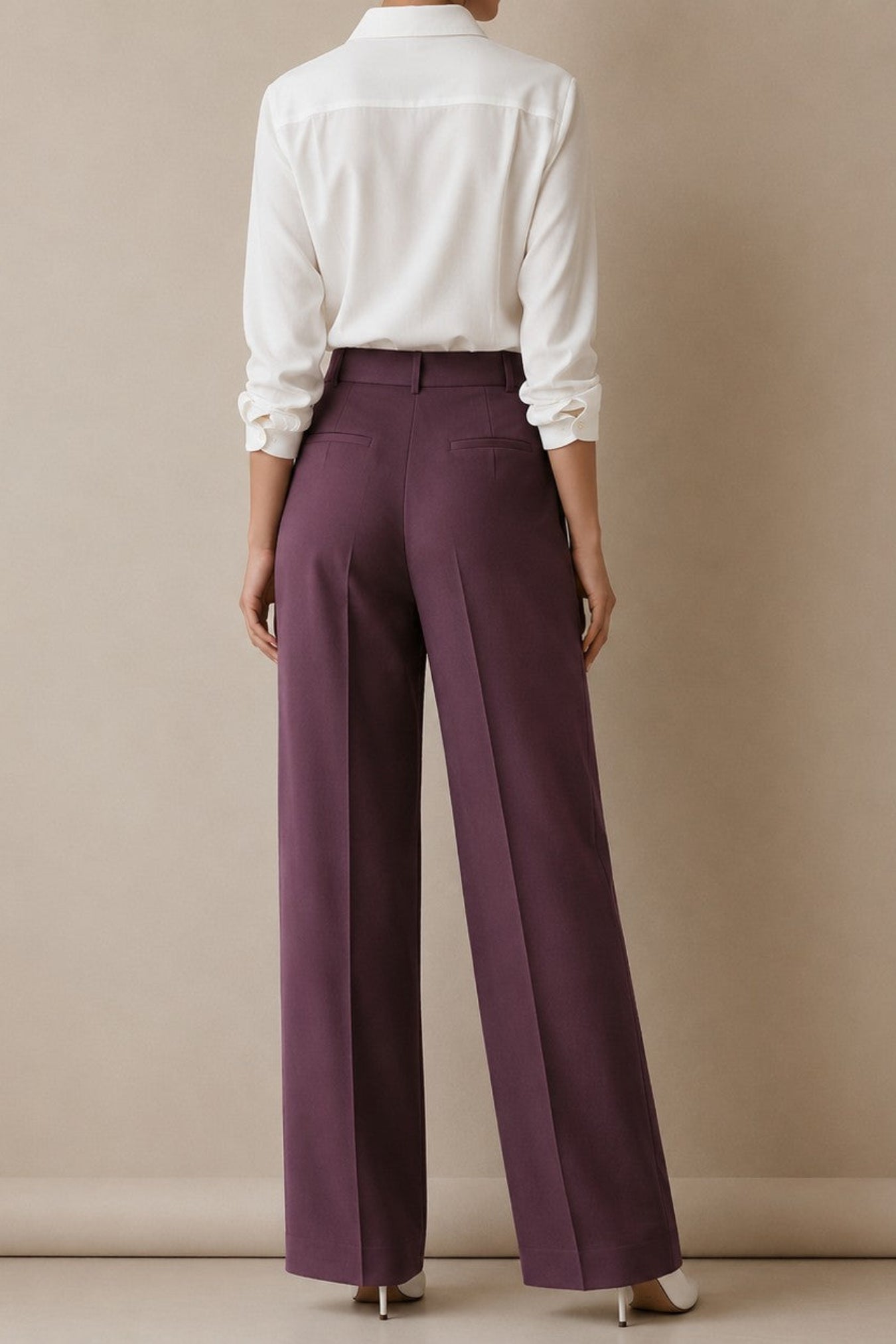 A model shown from the back wearing high-waisted, wide-leg trousers in a deep plum purple, paired with a white long-sleeve shirt and white heels, set against a plain beige studio background.