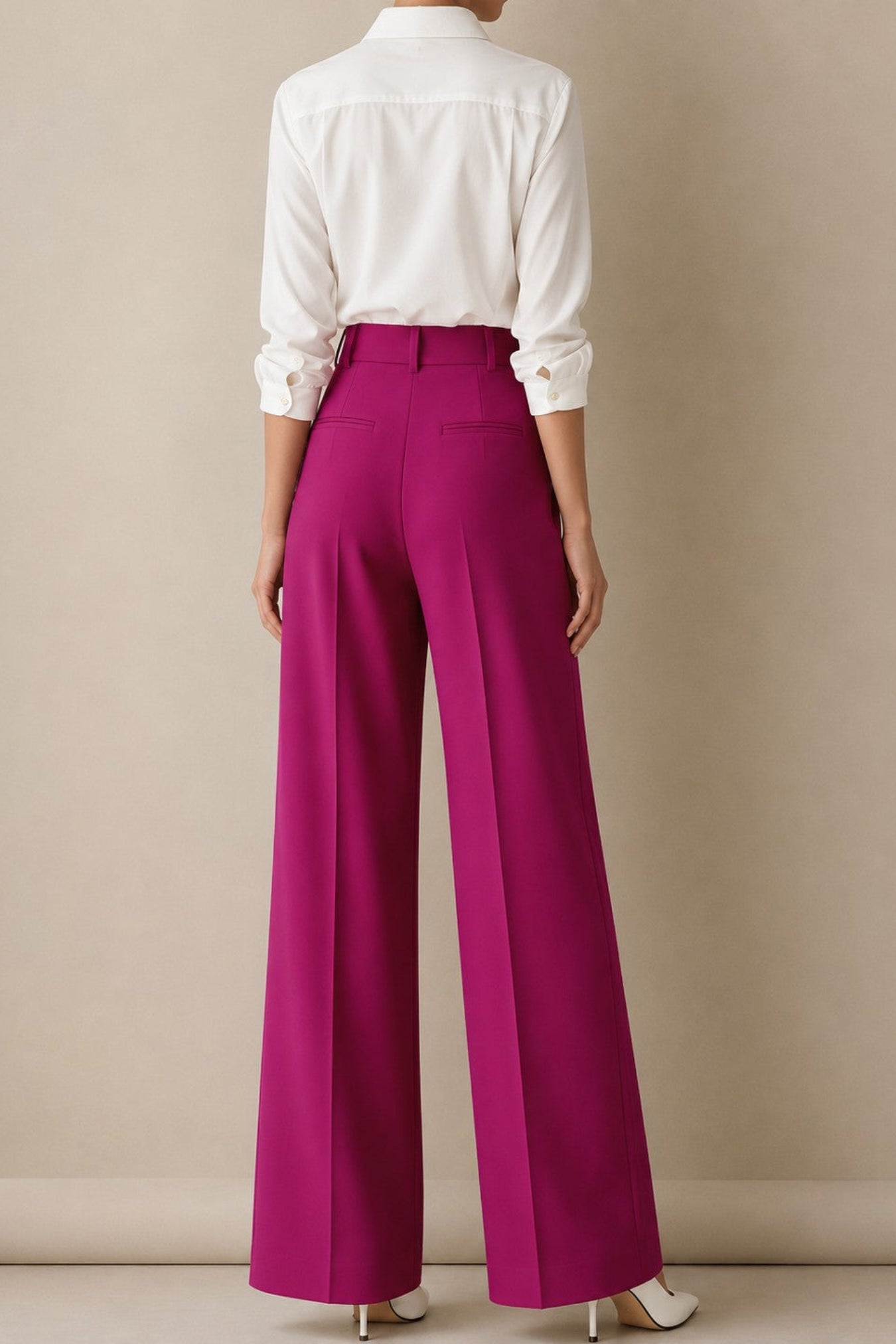 A model shown from the back wearing bright magenta wide-leg trousers and a white button-down shirt, standing against a neutral beige studio background.