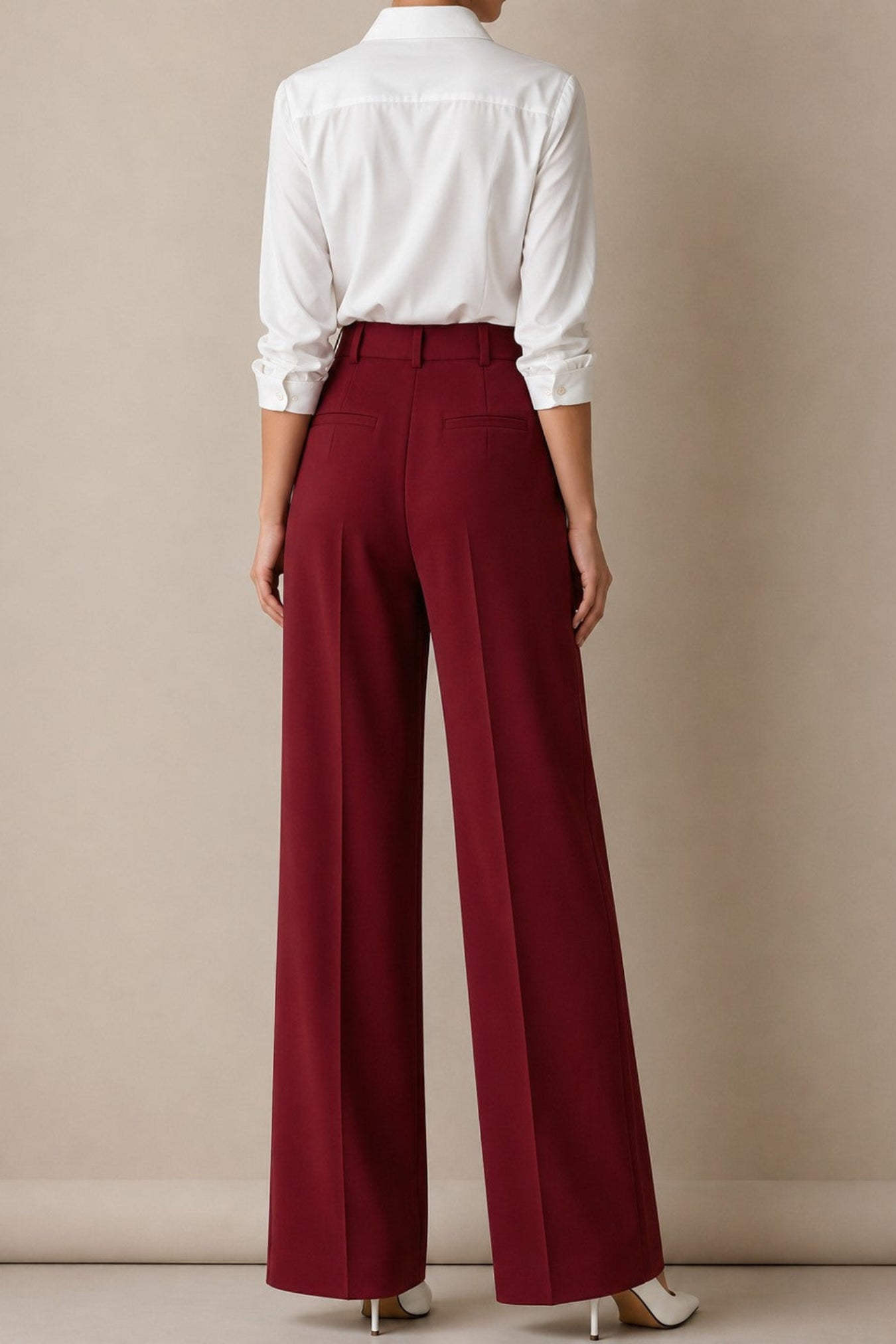 A model shown from the back wearing high-waisted, wide-leg burgundy trousers and a white long-sleeve button-down shirt, standing against a neutral beige studio background.