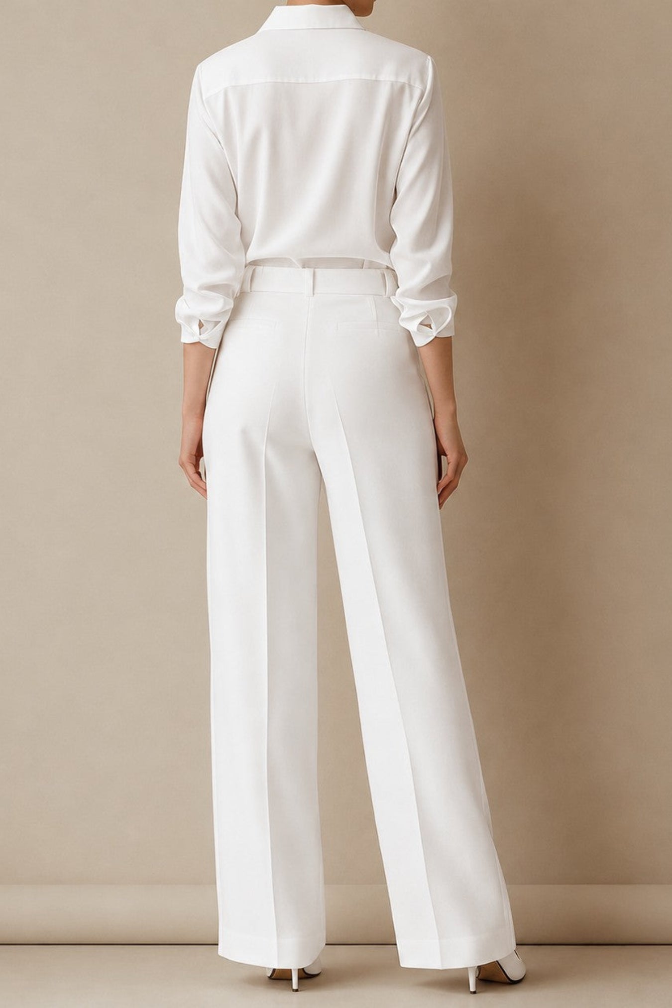A model shown from the back wearing a white long-sleeve button-up shirt and matching white wide-leg trousers, standing against a solid beige studio wall.