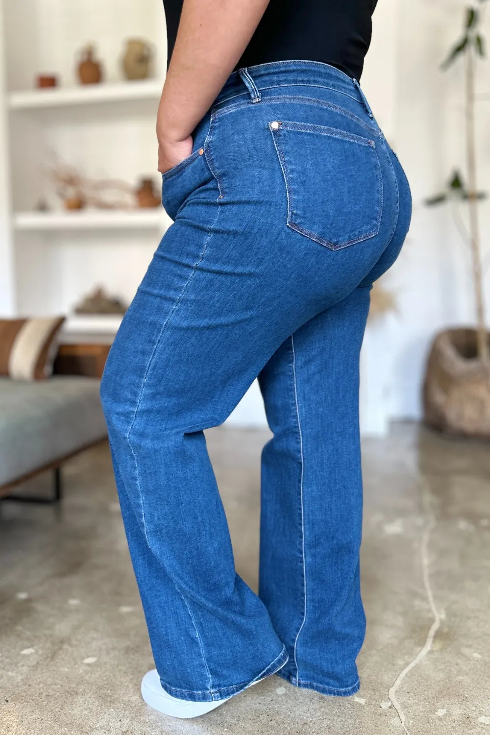 Person wearing blue jeans in a room with a shelf and plant in the background