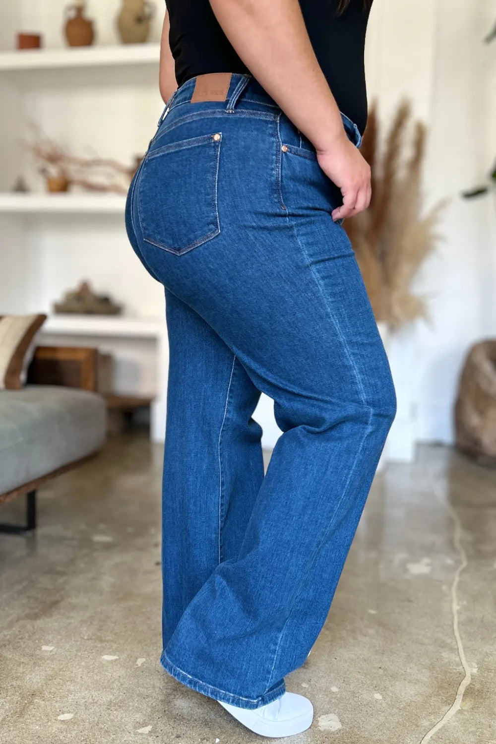 Person wearing blue jeans in a room with a white wall and decorative items.