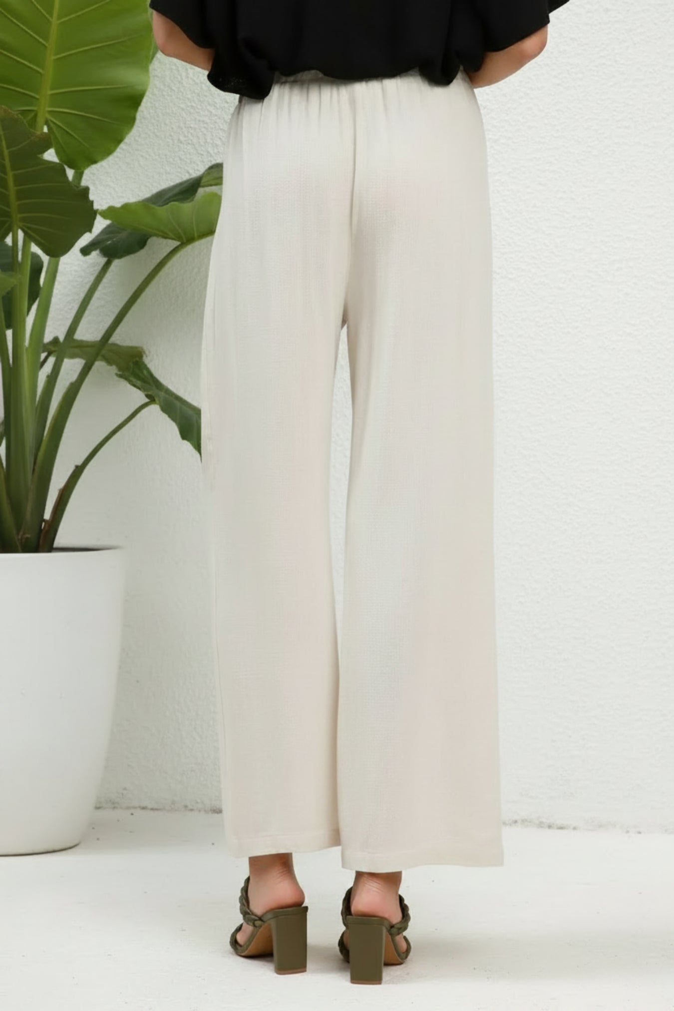 White wide-leg pants worn by a person on a white background next to a plant