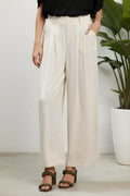 Person wearing oatmeal-colored wide-leg pants on a white background next to a potted plant