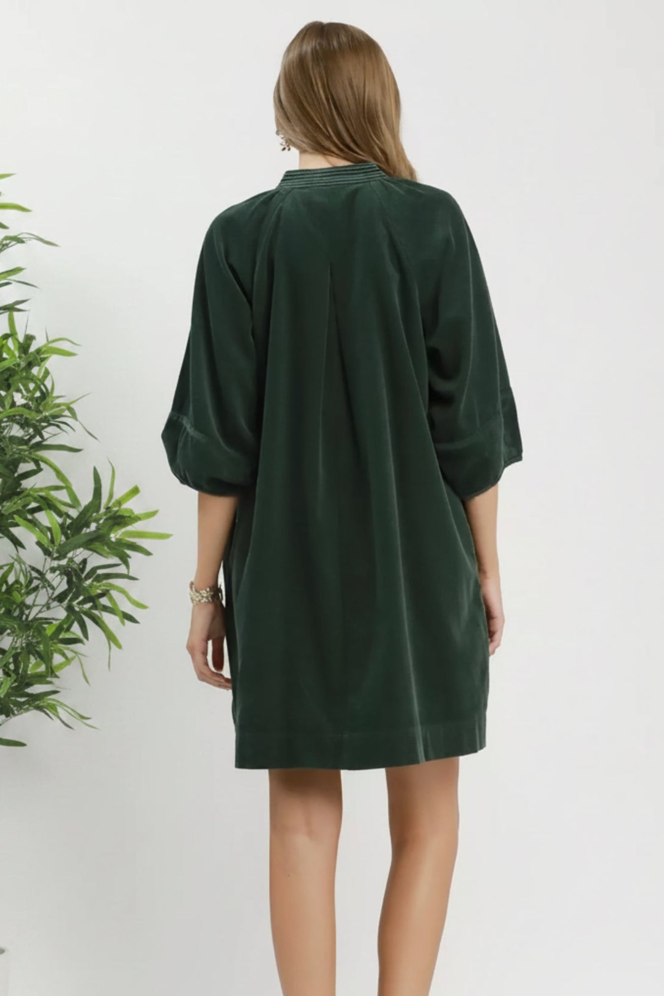 A woman shown from the back wearing an oversized dark green corduroy dress with three-quarter sleeves and brown ankle boots, against a white background.