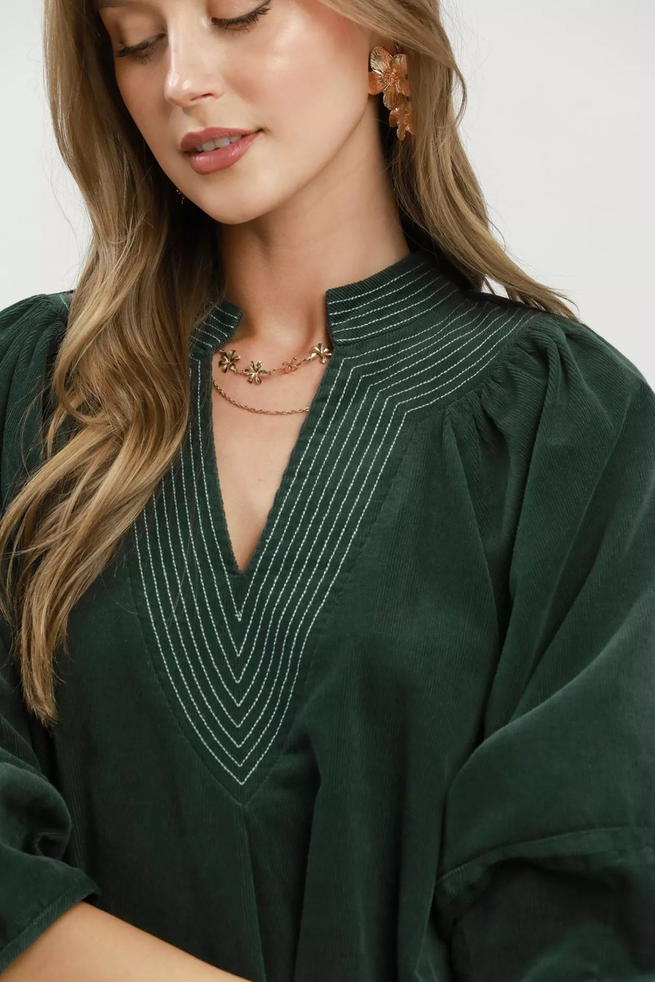 Woman wearing a hunter green blouse with intricate detailing on a plain background