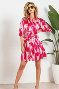Woman wearing a pink and white patterned dress with sunglasses on a white background